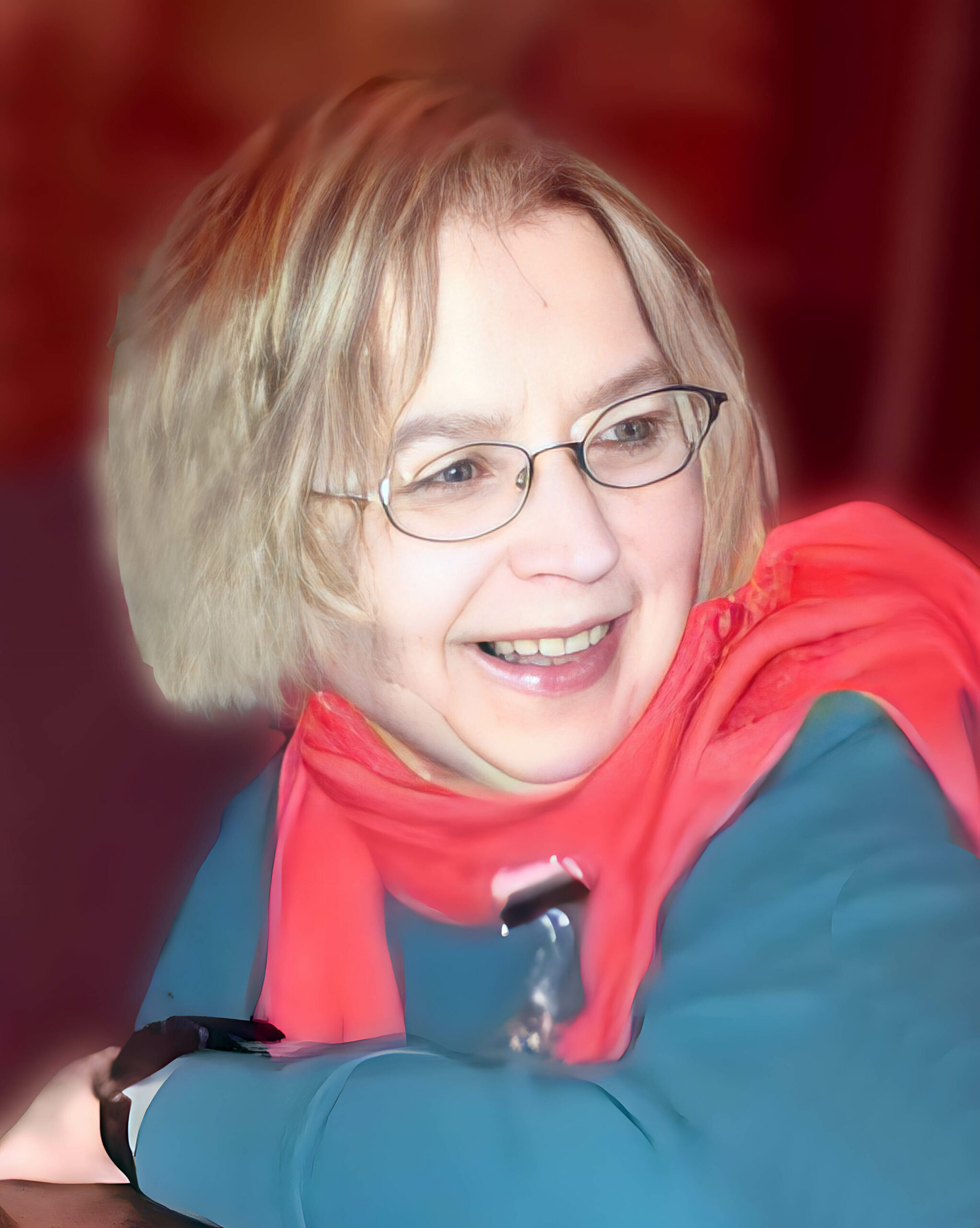 Smiling woman wearing glasses and a bright red scarf, looking to the side against a blurred red background.