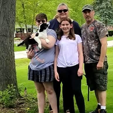 Family of four with a black-and-white dog posing together in a sunny park.
