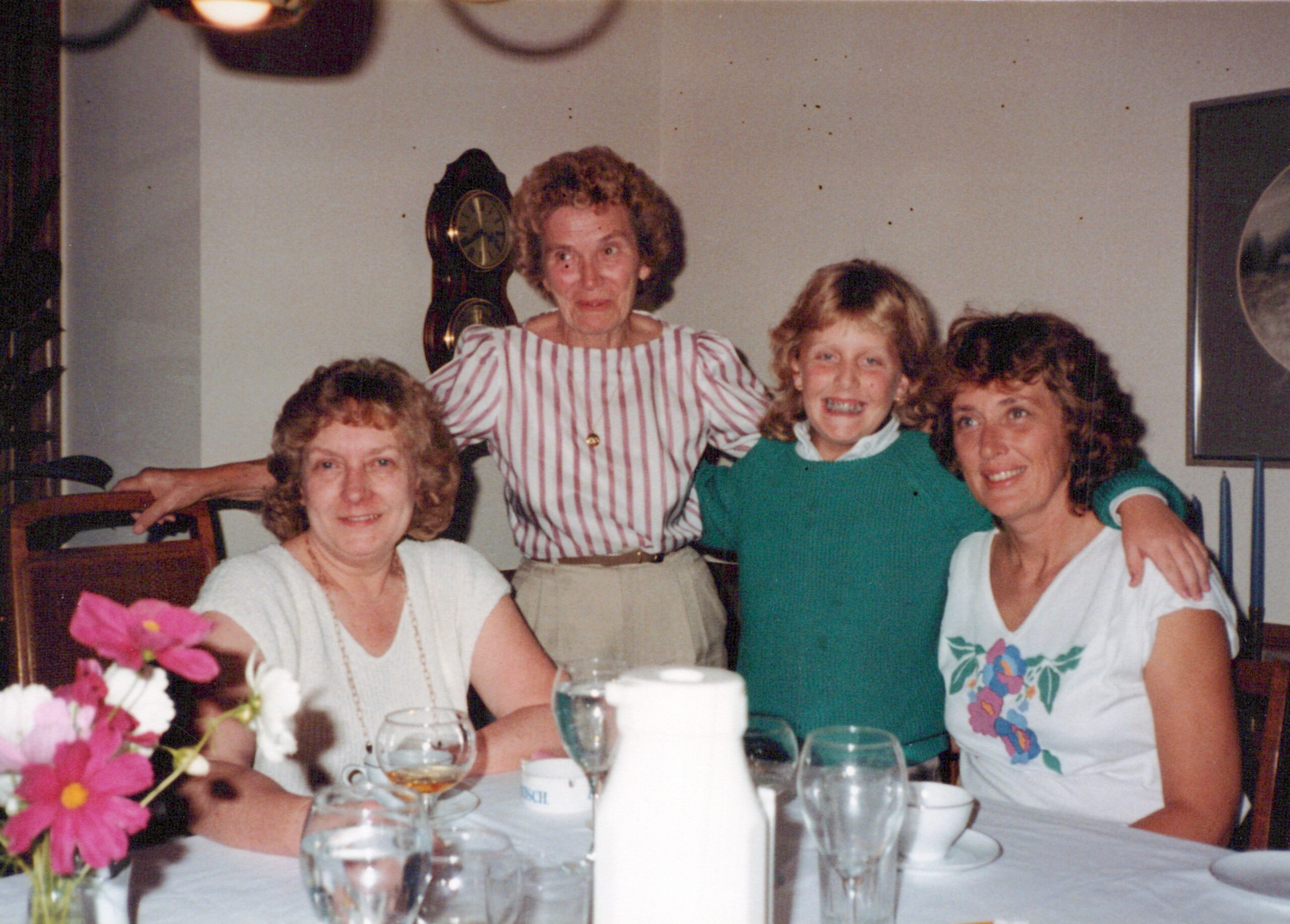 Group of four people seated together at a dining table, smiling for the camera, with flowers and drinks in the foreground.