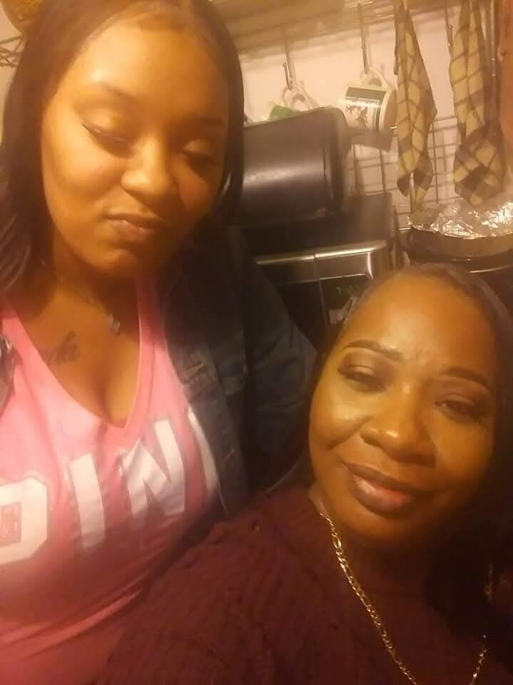 Two women posing for a selfie in a warm-lit kitchen, smiling at the camera.