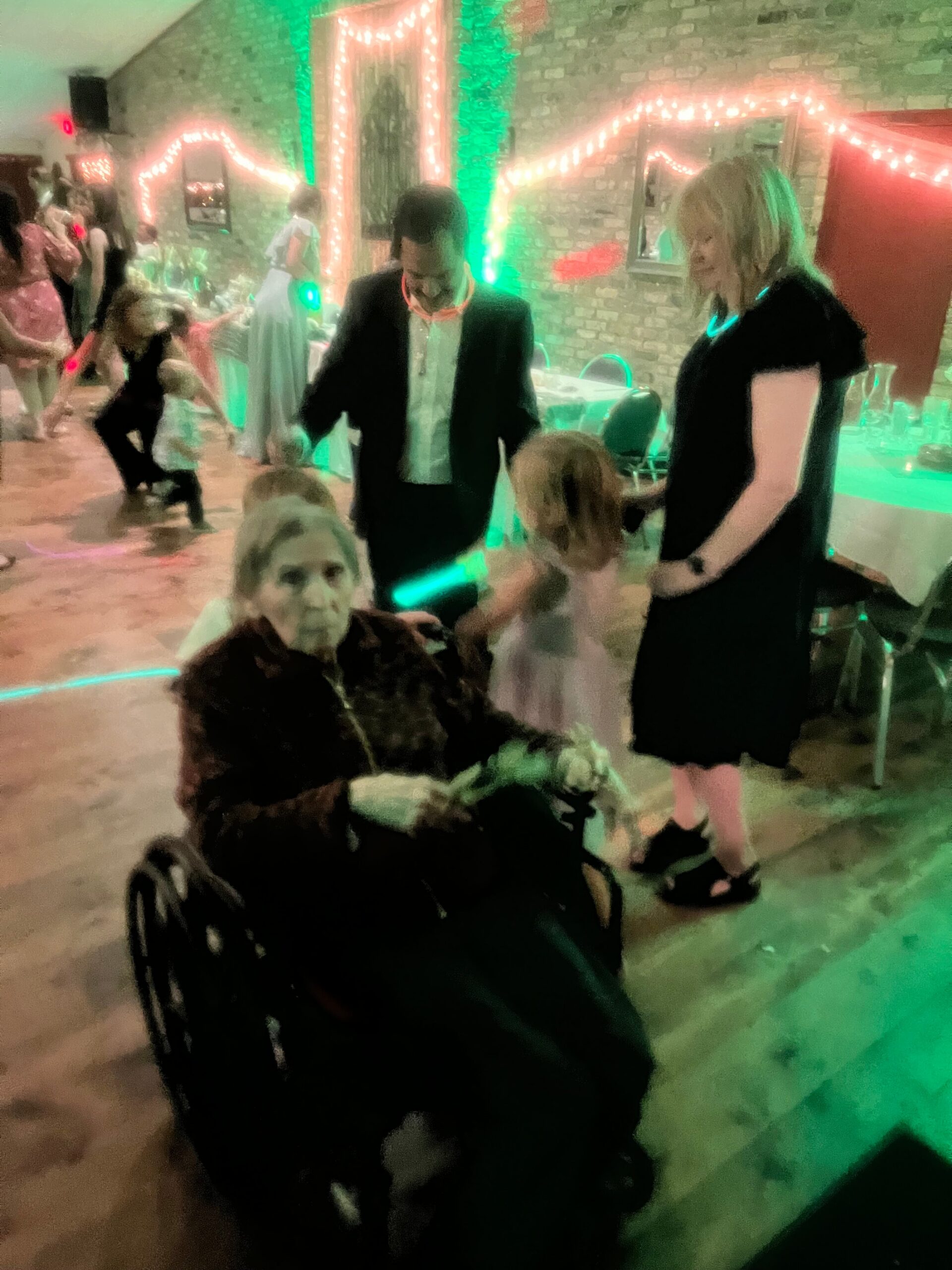 People dancing at a party in a brick-walled venue with green and pink lighting.