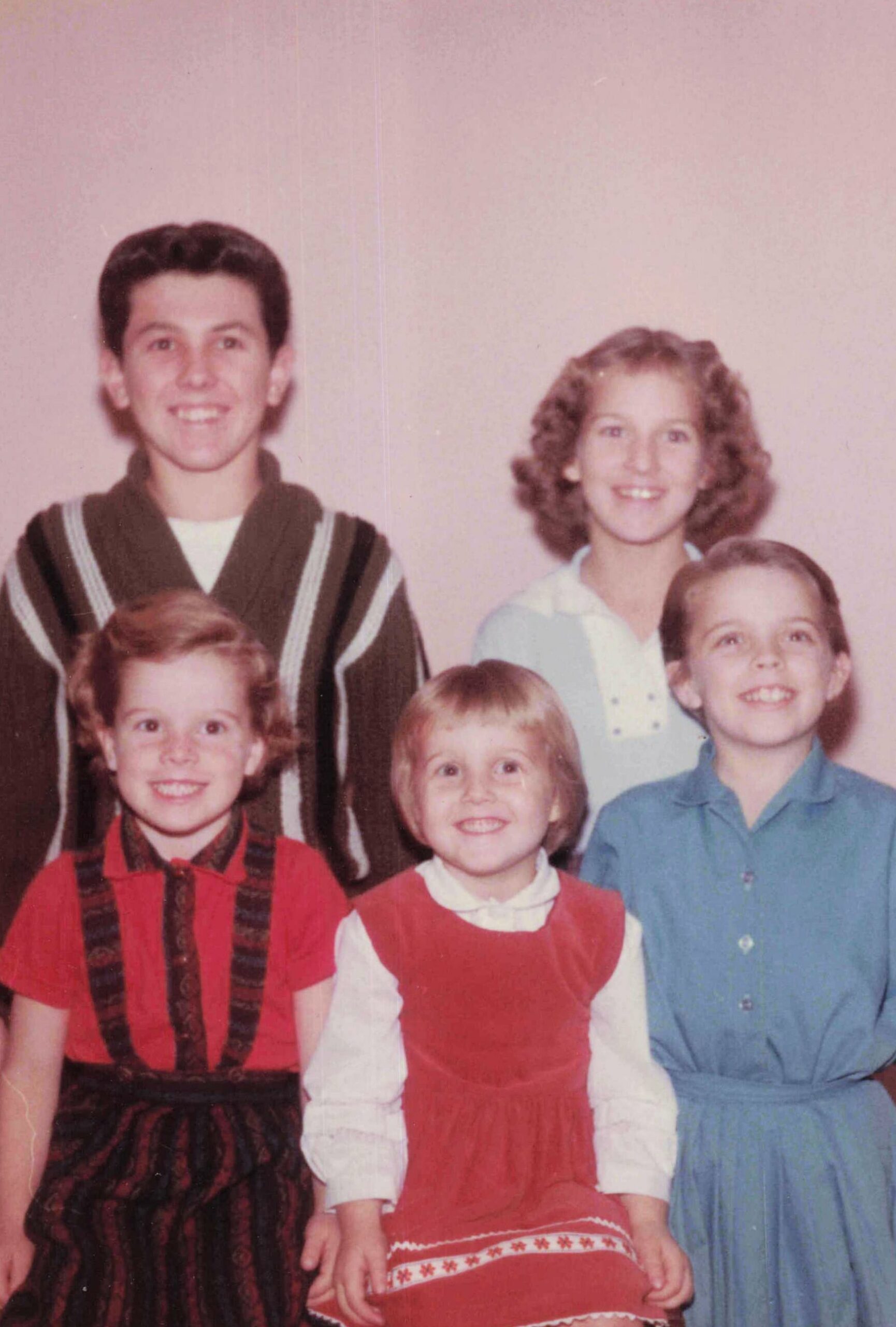Smiling family group photo with children in festive red and blue outfits and two adults in the back, posed indoors.