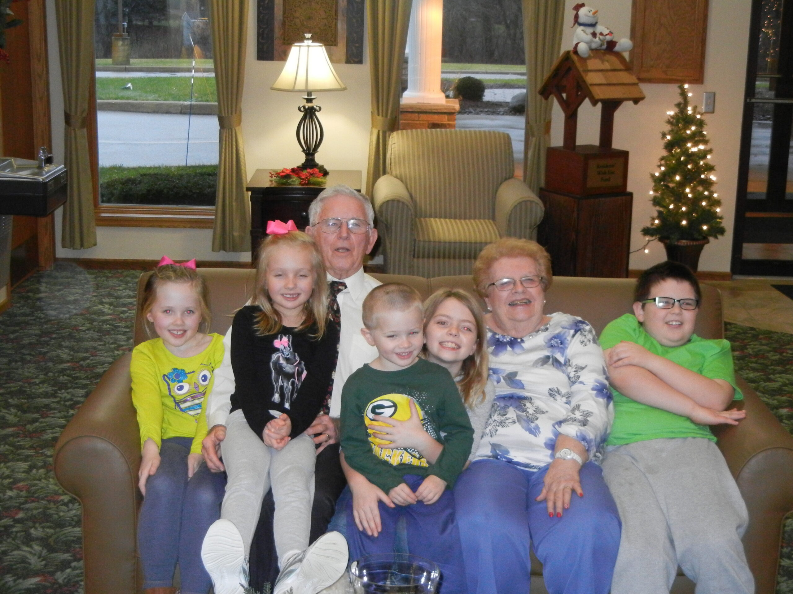 Group of children and adults posing on a sofa in a Christmas-themed living room with holiday decorations in the background.
