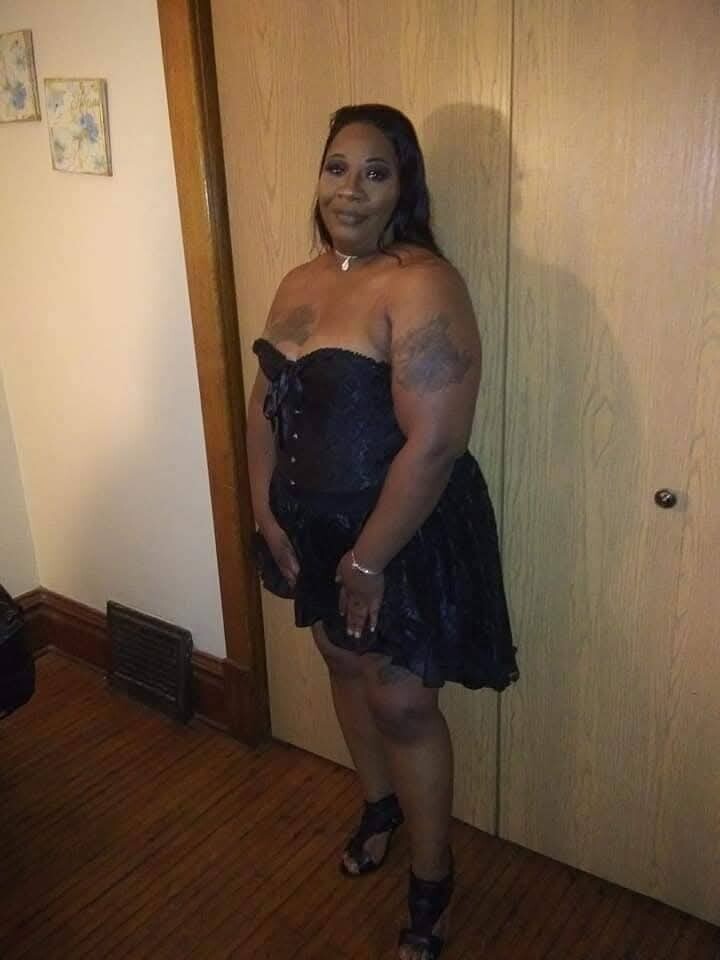 Woman in a black strapless corset dress and heels stands in a doorway.