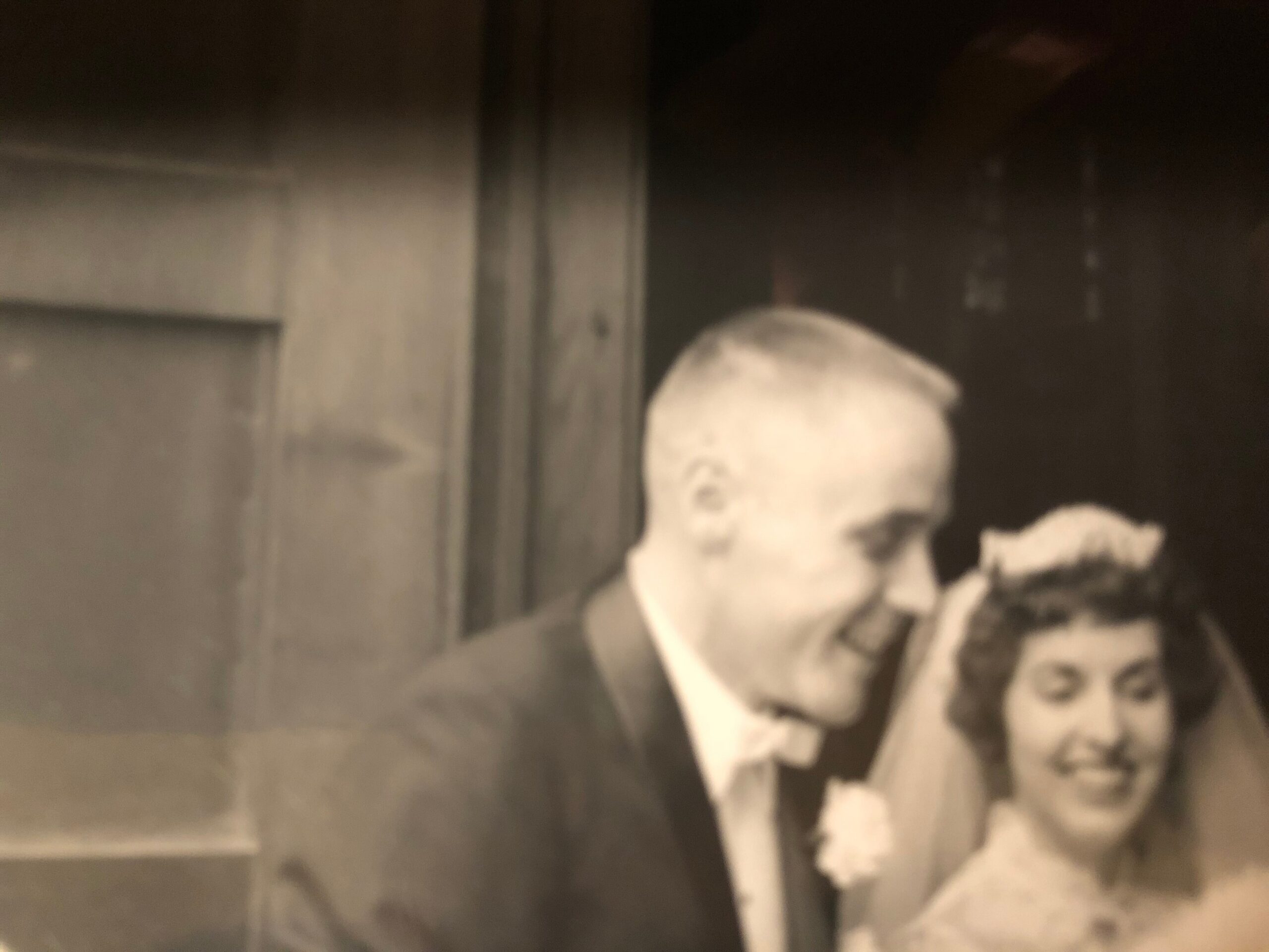 Low-light photo of a person wearing a light patterned scarf, partially visible on the right side of the frame near a doorway.