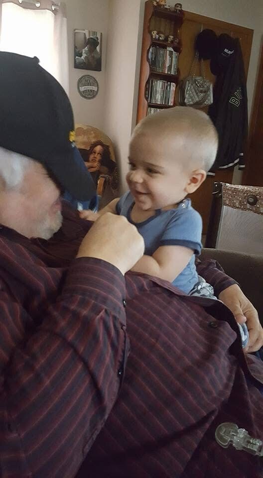 Smiling baby sitting on an older man's lap indoors, they share a playful moment.
