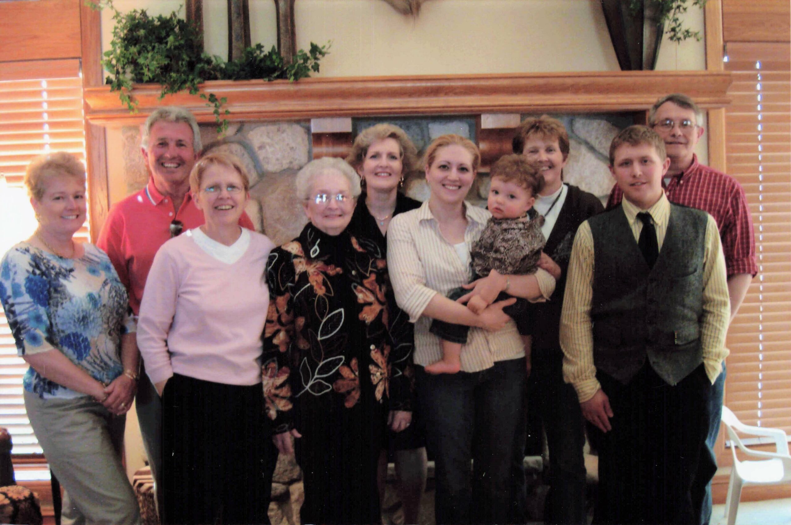 Group of eleven people posing together indoors in front of a stone fireplace, all smiling.
