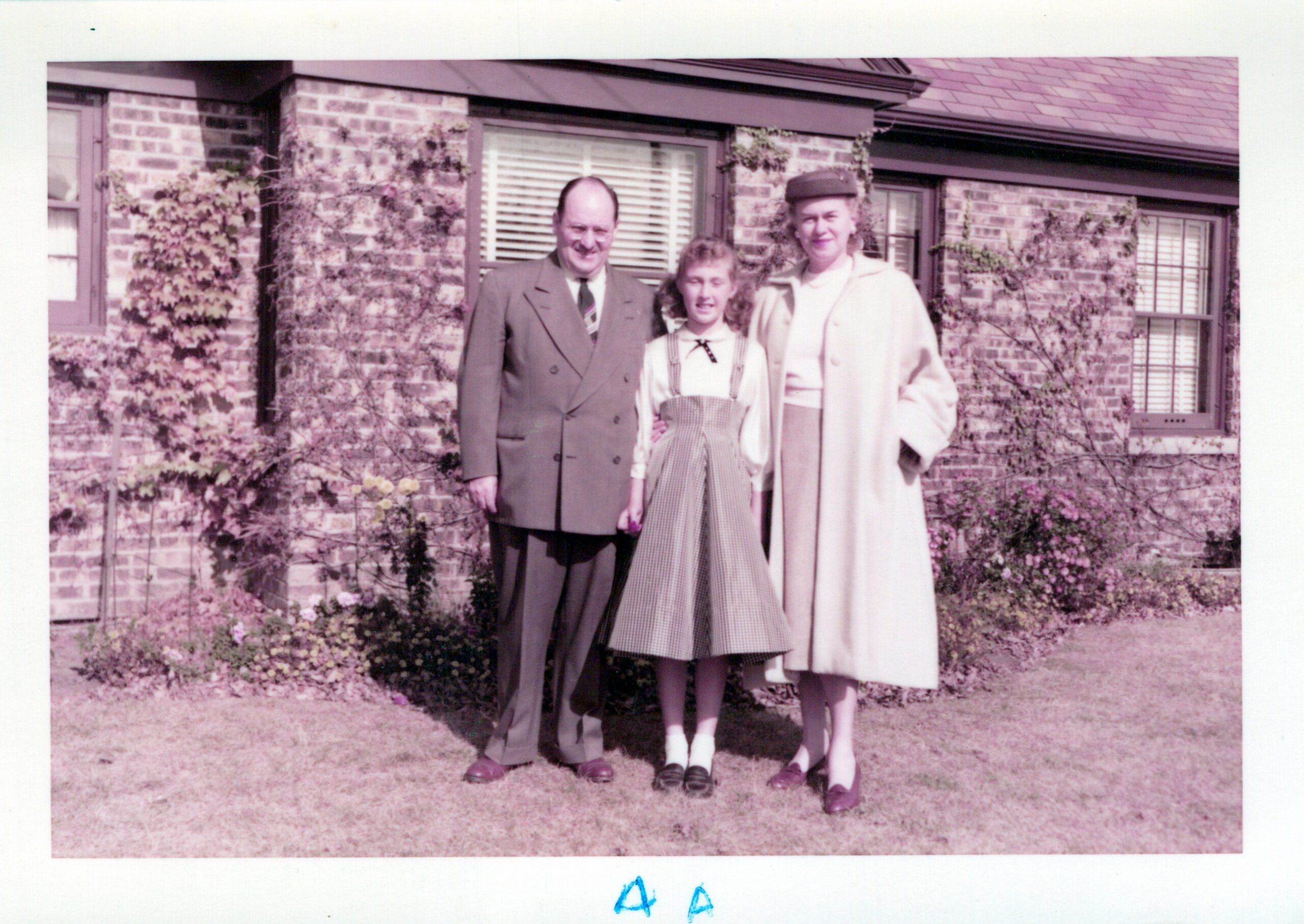 Family of three posing outside a brick house in 1950s attire.