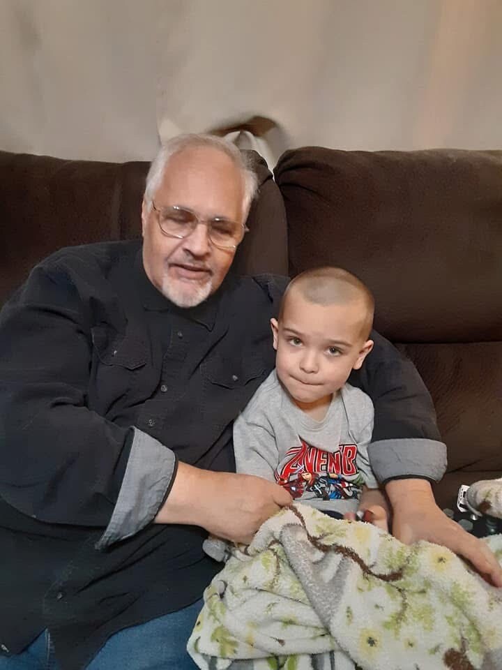 Grandfather with glasses sitting on a brown couch beside a young boy, wrapped in a blanket.