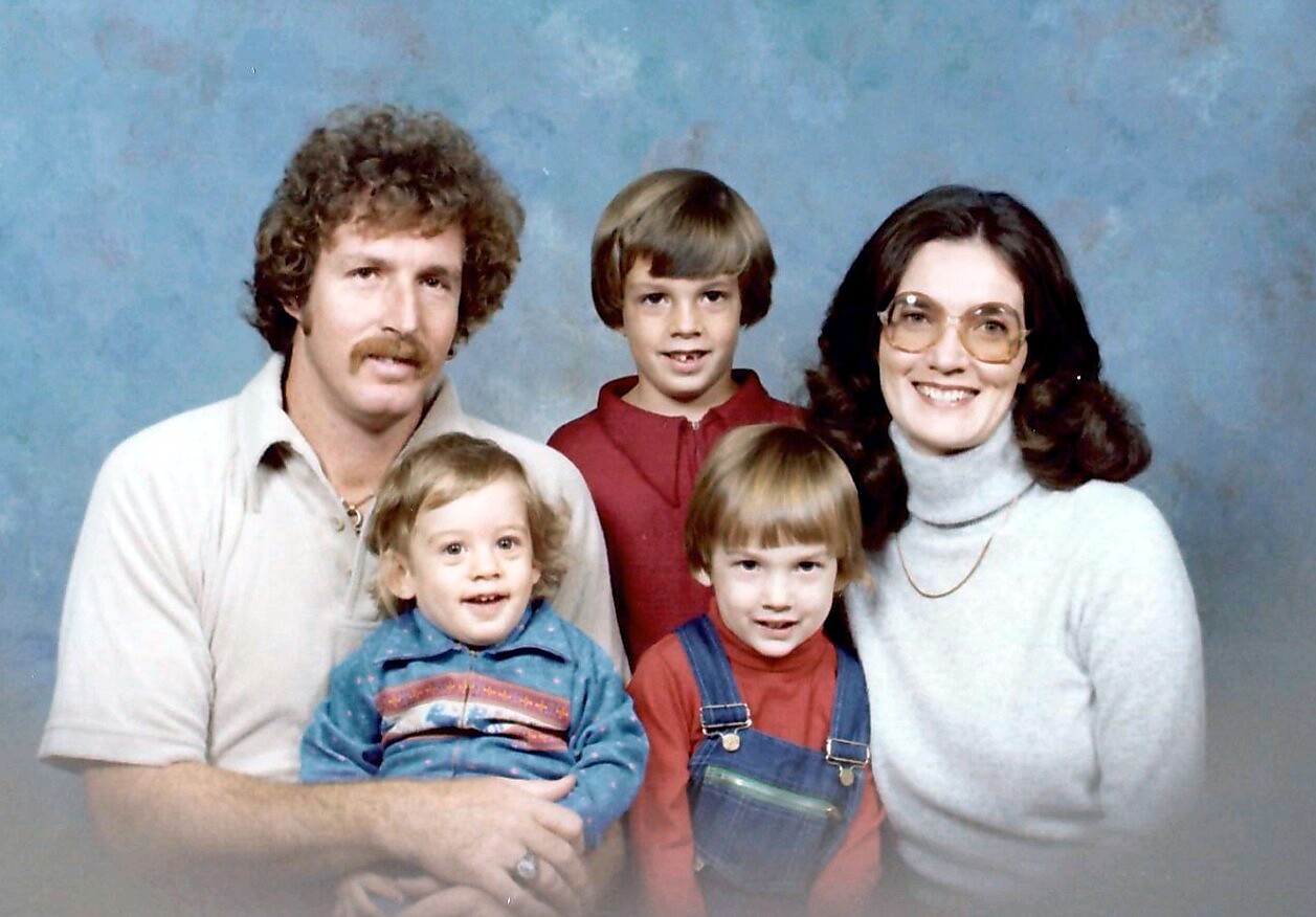 Family portrait of a father, mother, and three young children posing together in a studio with a blue backdrop.