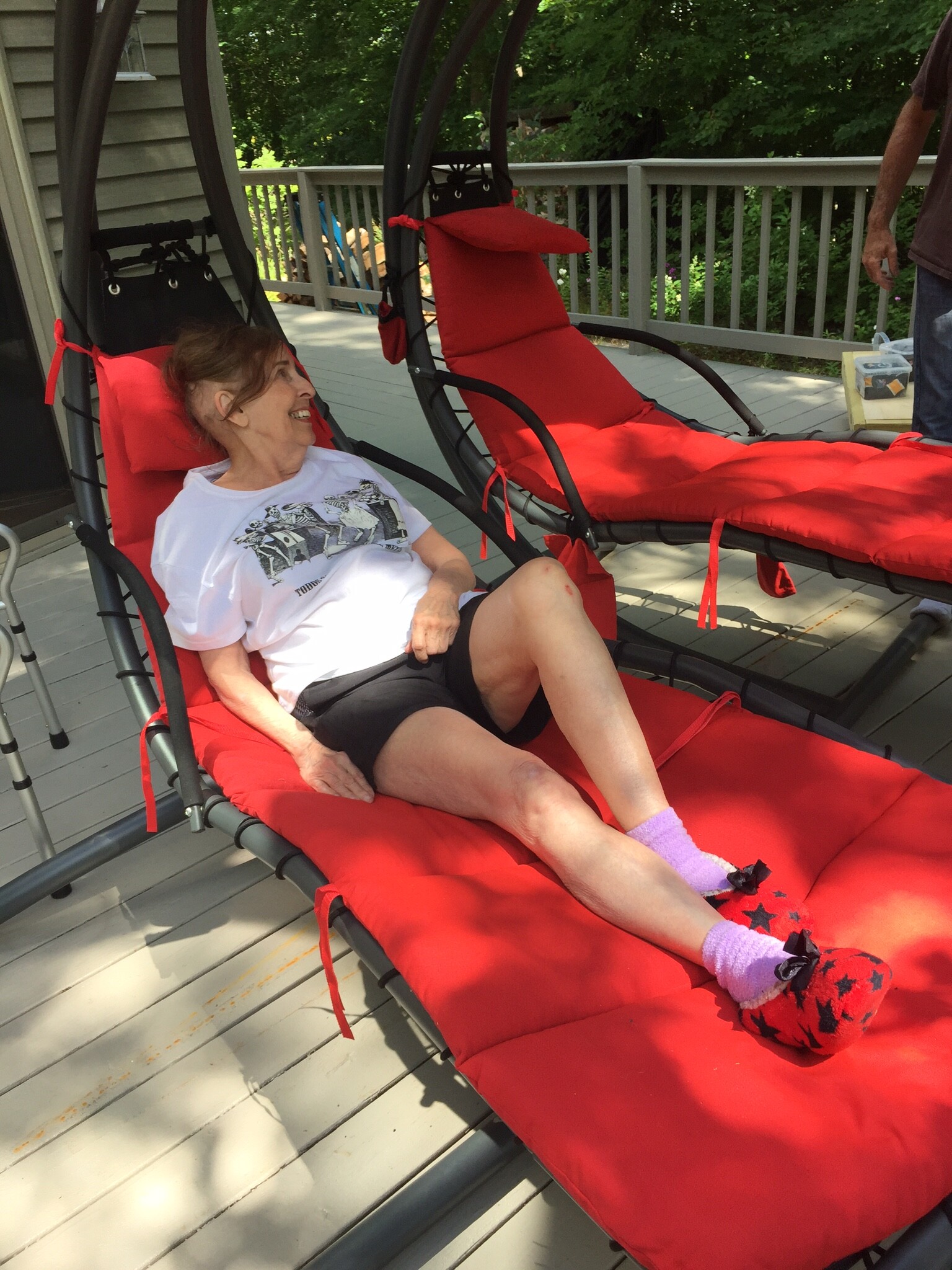 Older woman relaxing on a red outdoor lounge chair on a wooden deck, smiling.