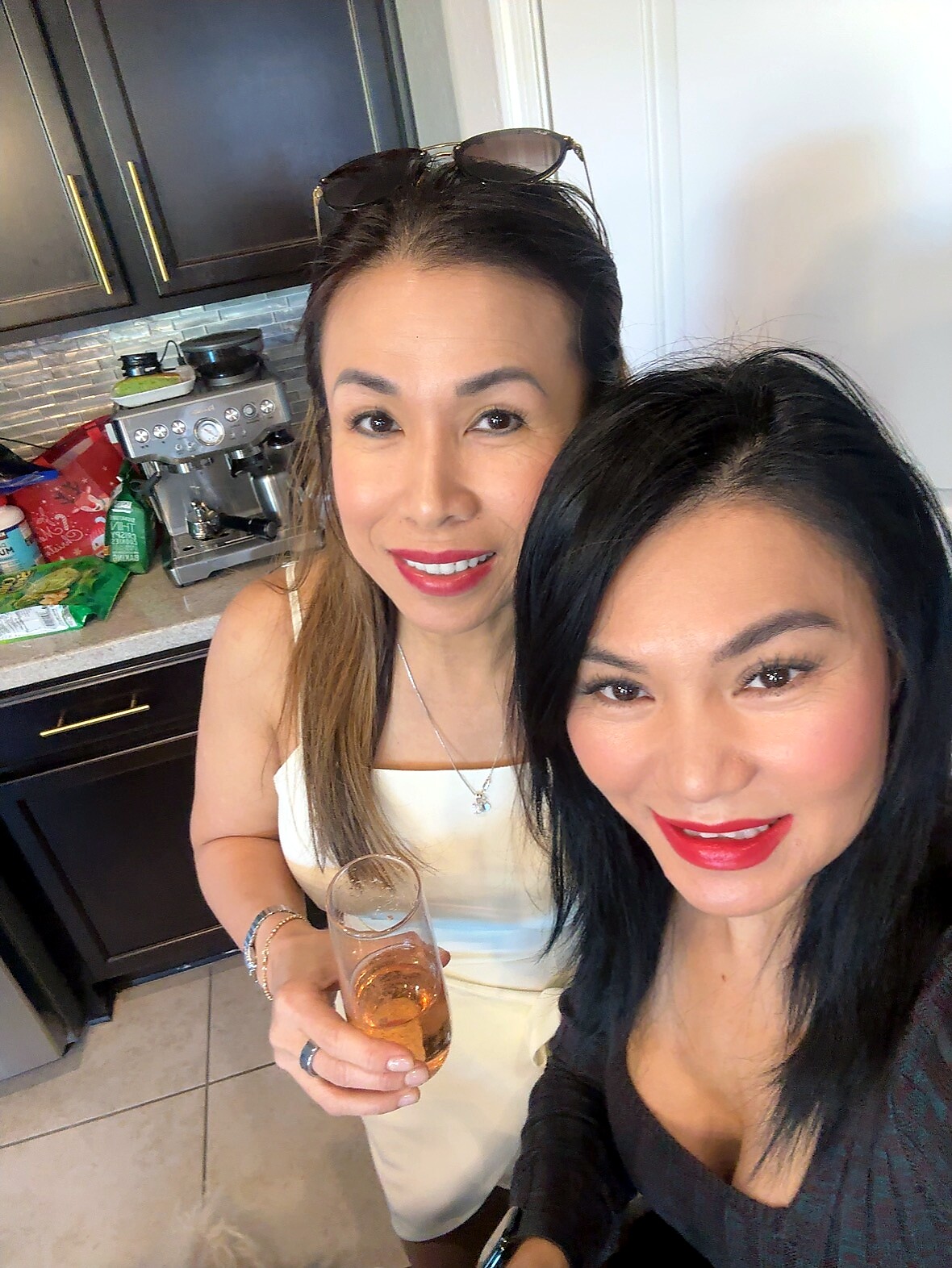 Two women in a kitchen take a selfie, smiling at the camera, one holding a champagne flute.