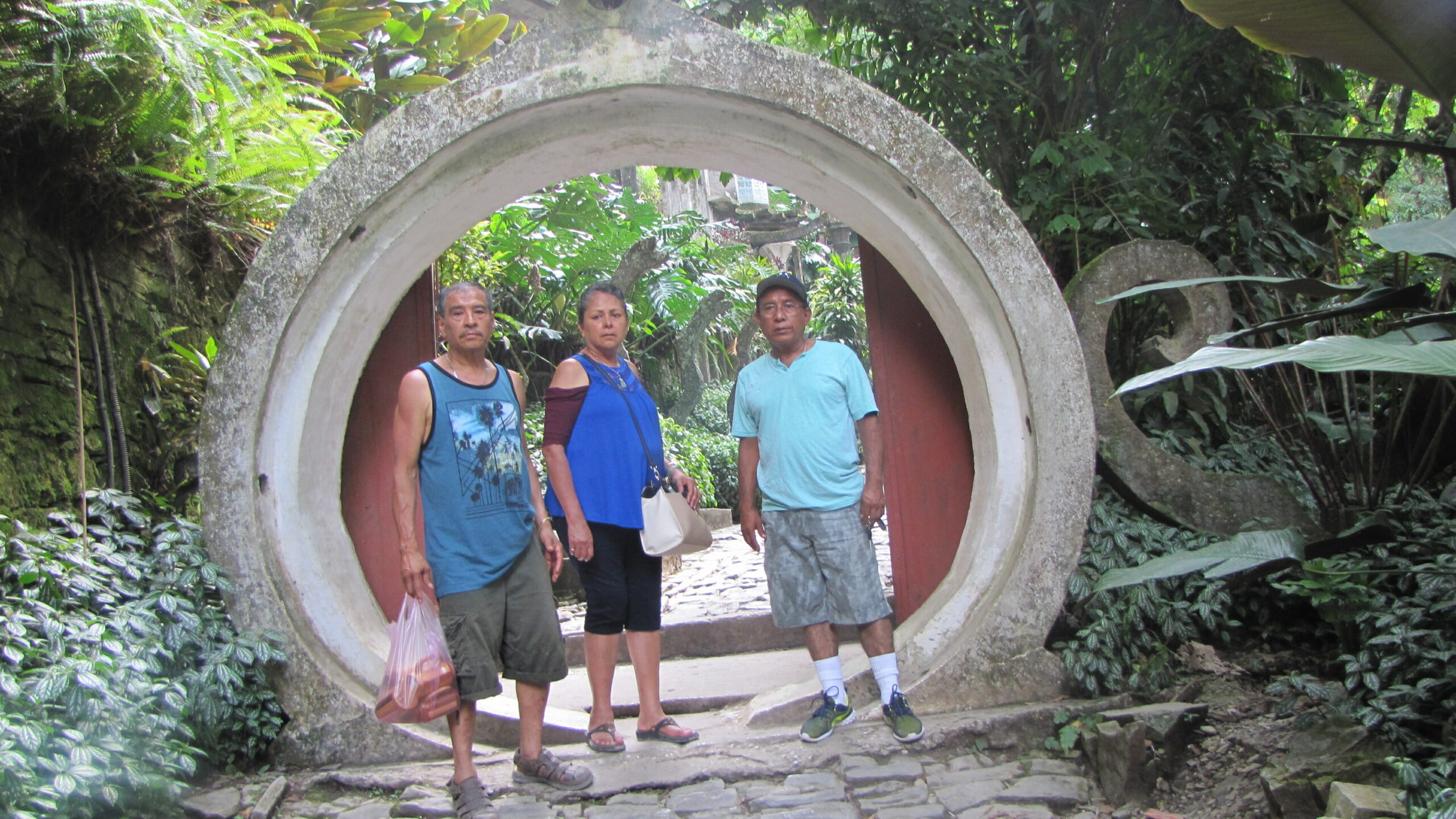 Three adults standing inside a large circular concrete tunnel in a lush garden setting.