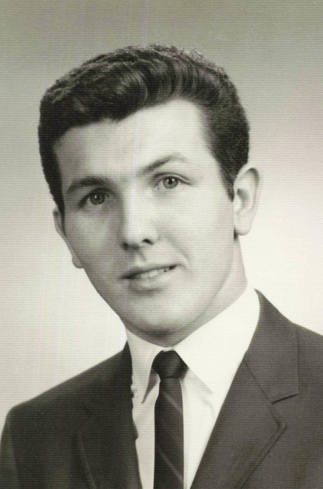 Black-and-white portrait of a young man in a suit and tie, smiling slightly at the camera.