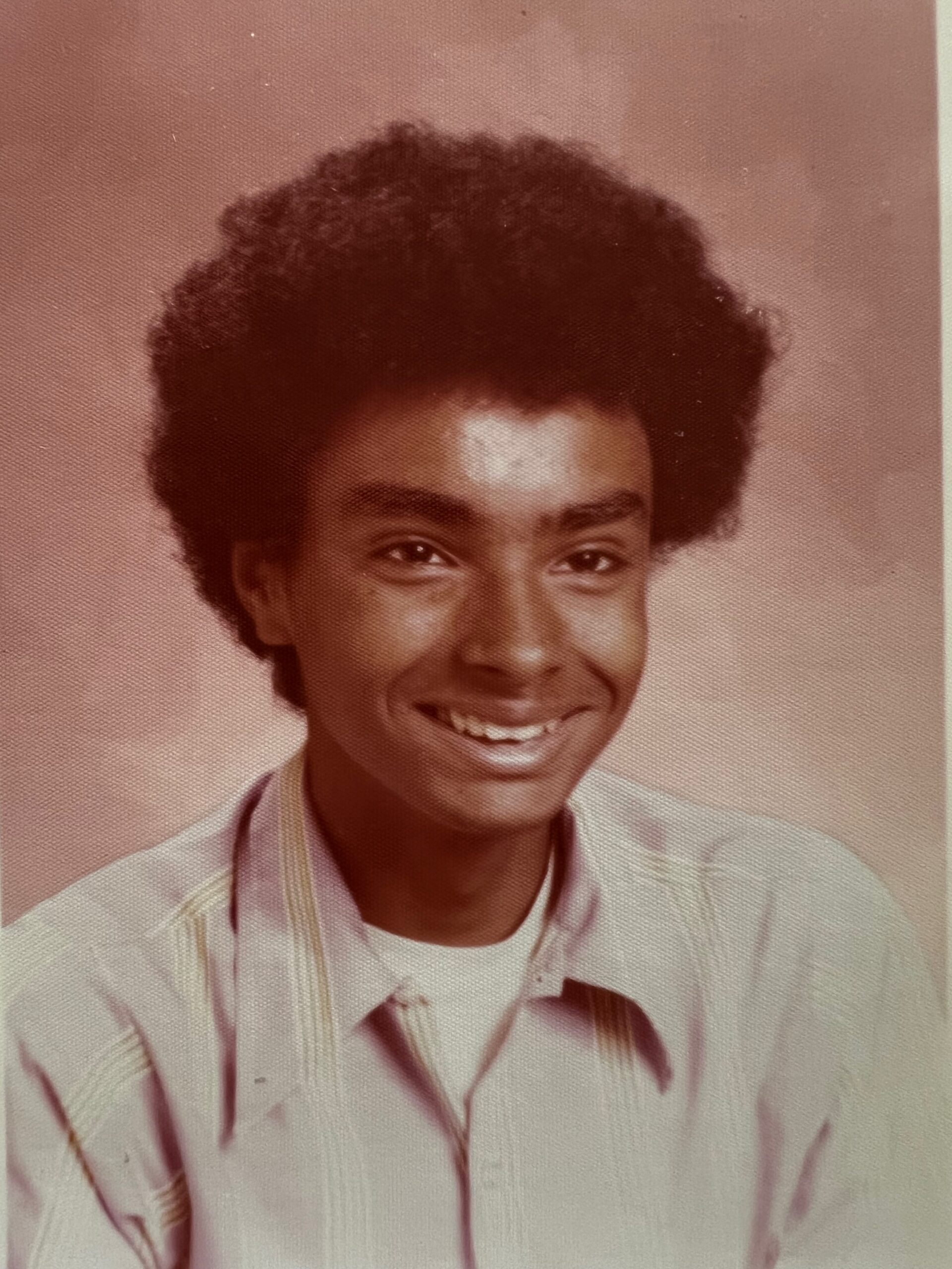 Young man with a large afro hairstyle smiling for a portrait in a light striped shirt.