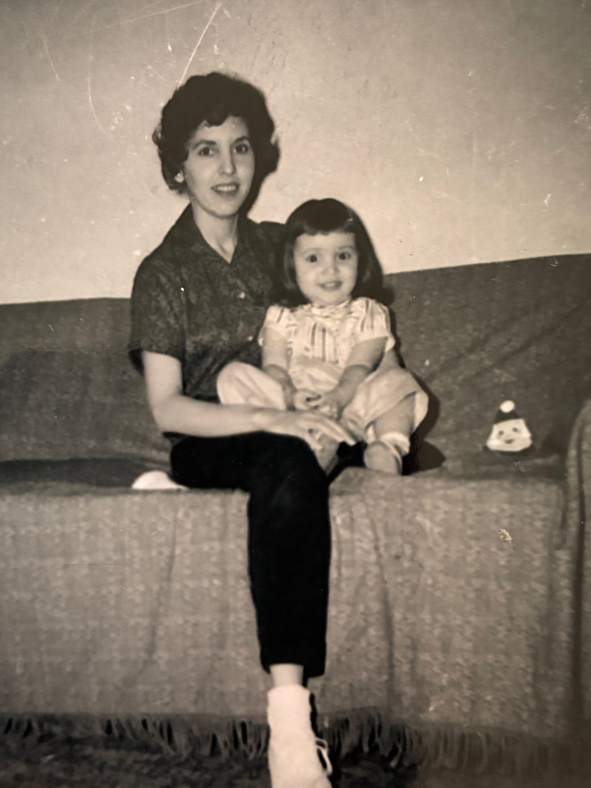 Woman with short dark hair sits beside a smiling young girl on a sofa in a black-and-white family photo.