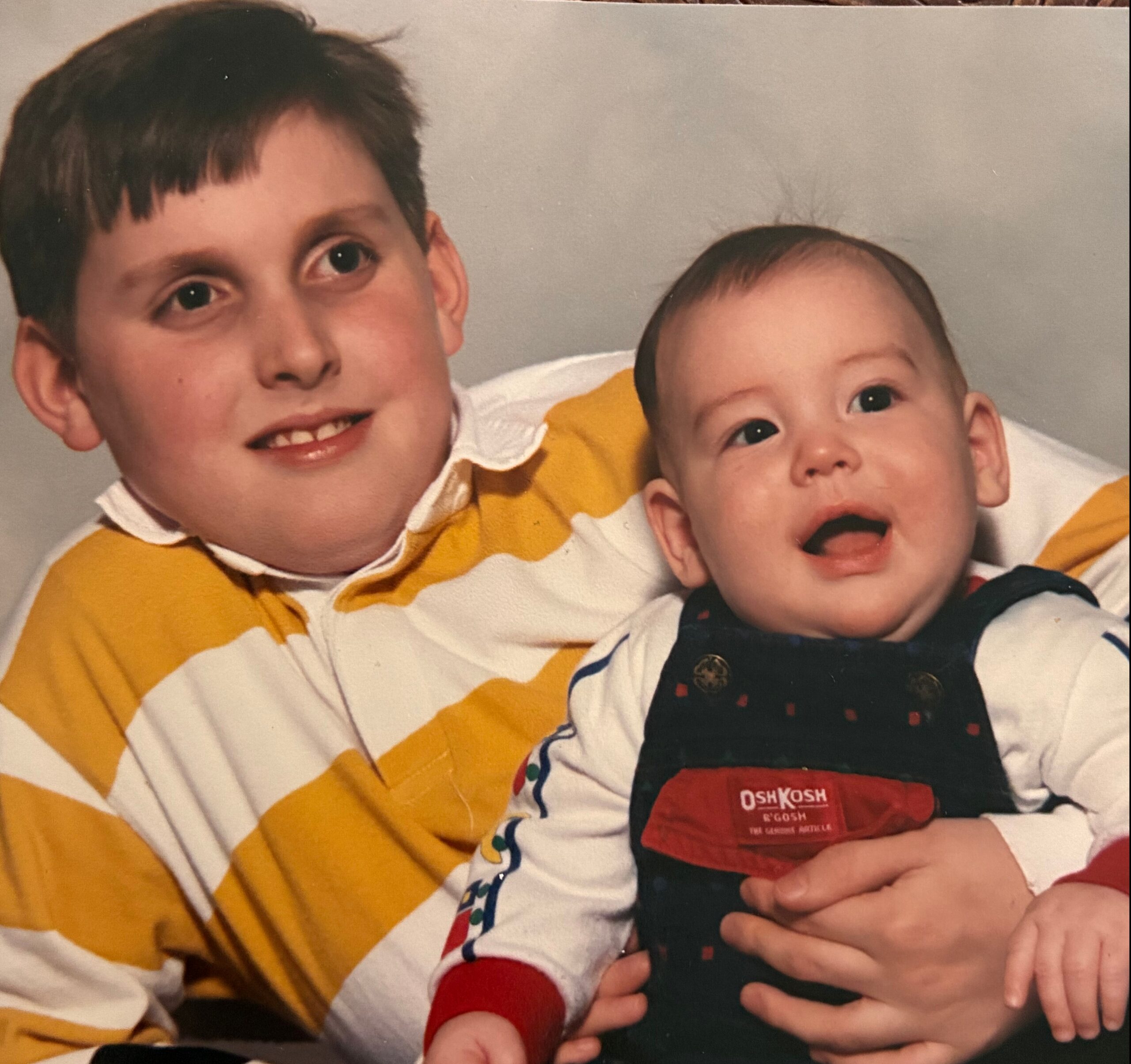 Smiling older boy cradling a baby, both wearing yellow-and-white striped outfits.