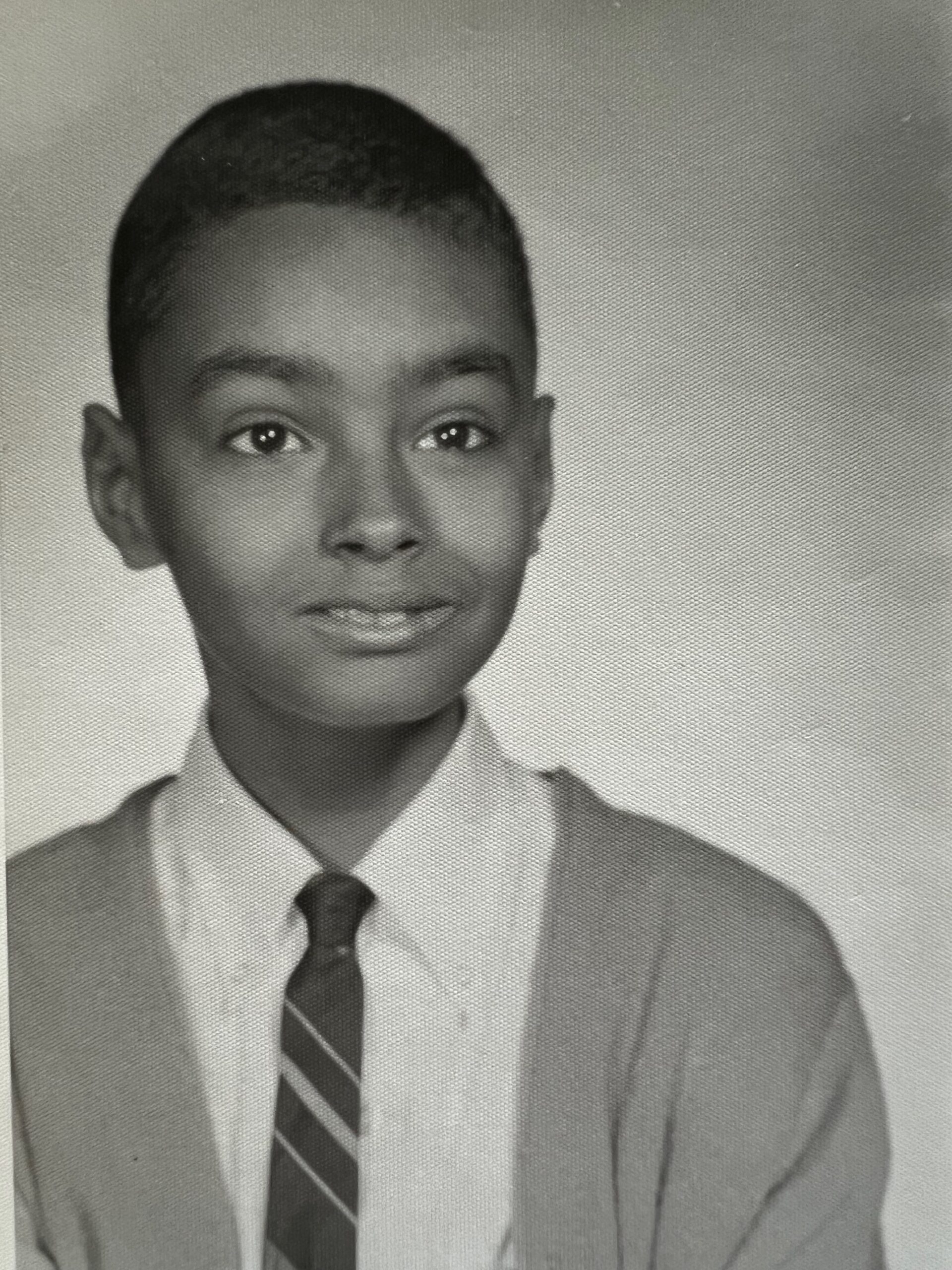 Young person in a blazer and striped tie, looking at the camera (black-and-white portrait)