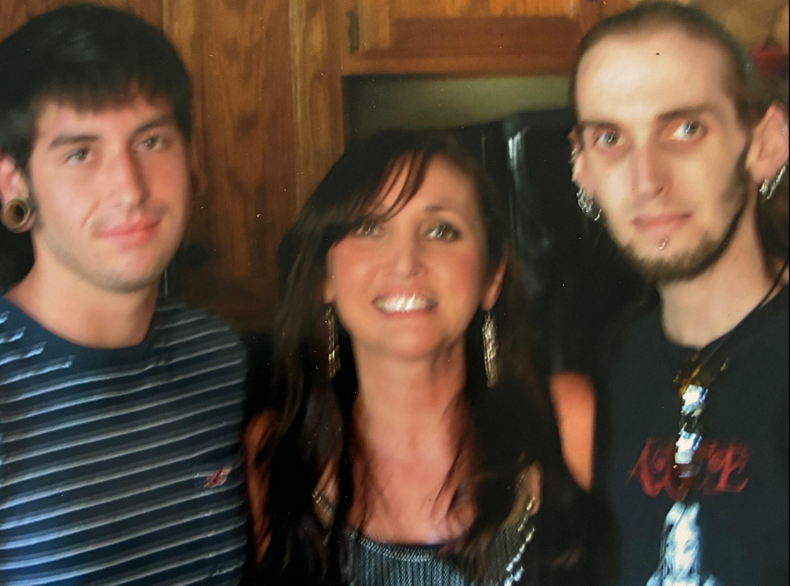 Three people posing for a close-up group photo indoors, smiling at the camera against a wooden background
