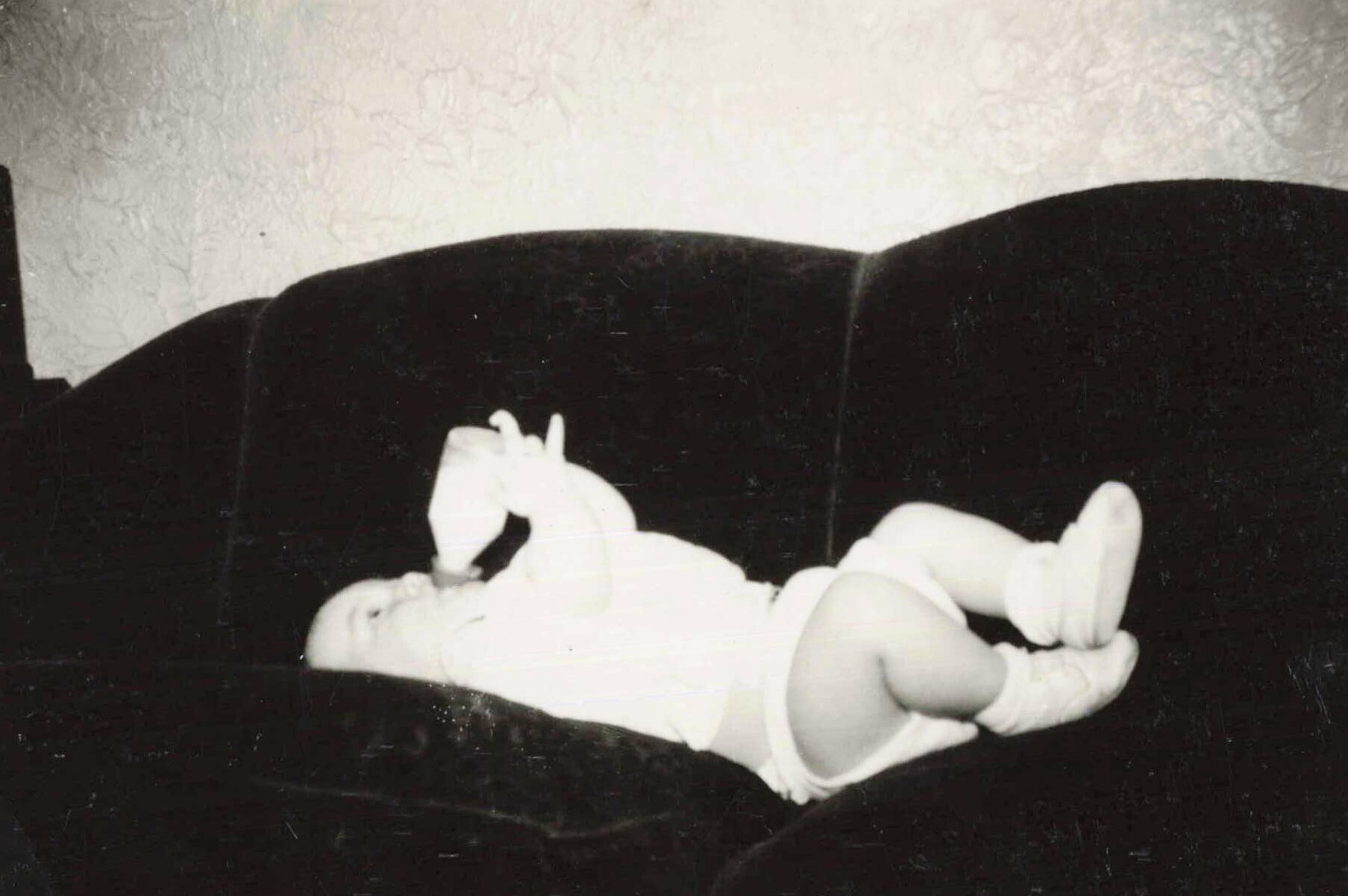 Black-and-white photo of a newborn baby lying on a dark surface, tiny hands near the face.
