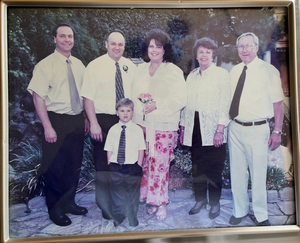 Bride in white holding flowers, surrounded by family outdoors on a stone path.