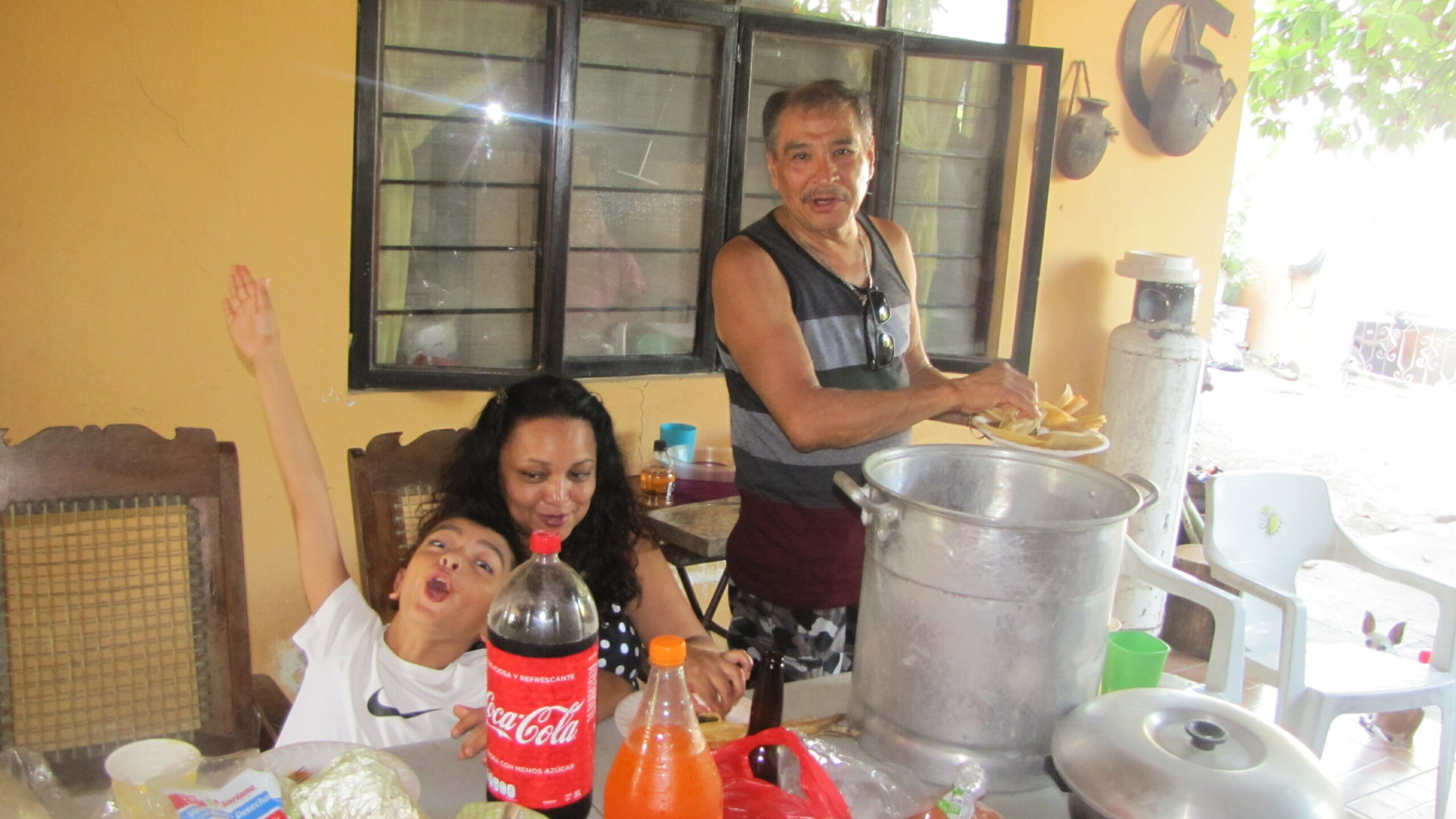 Man serving food from a large pot to a family at a patio table outdoors.