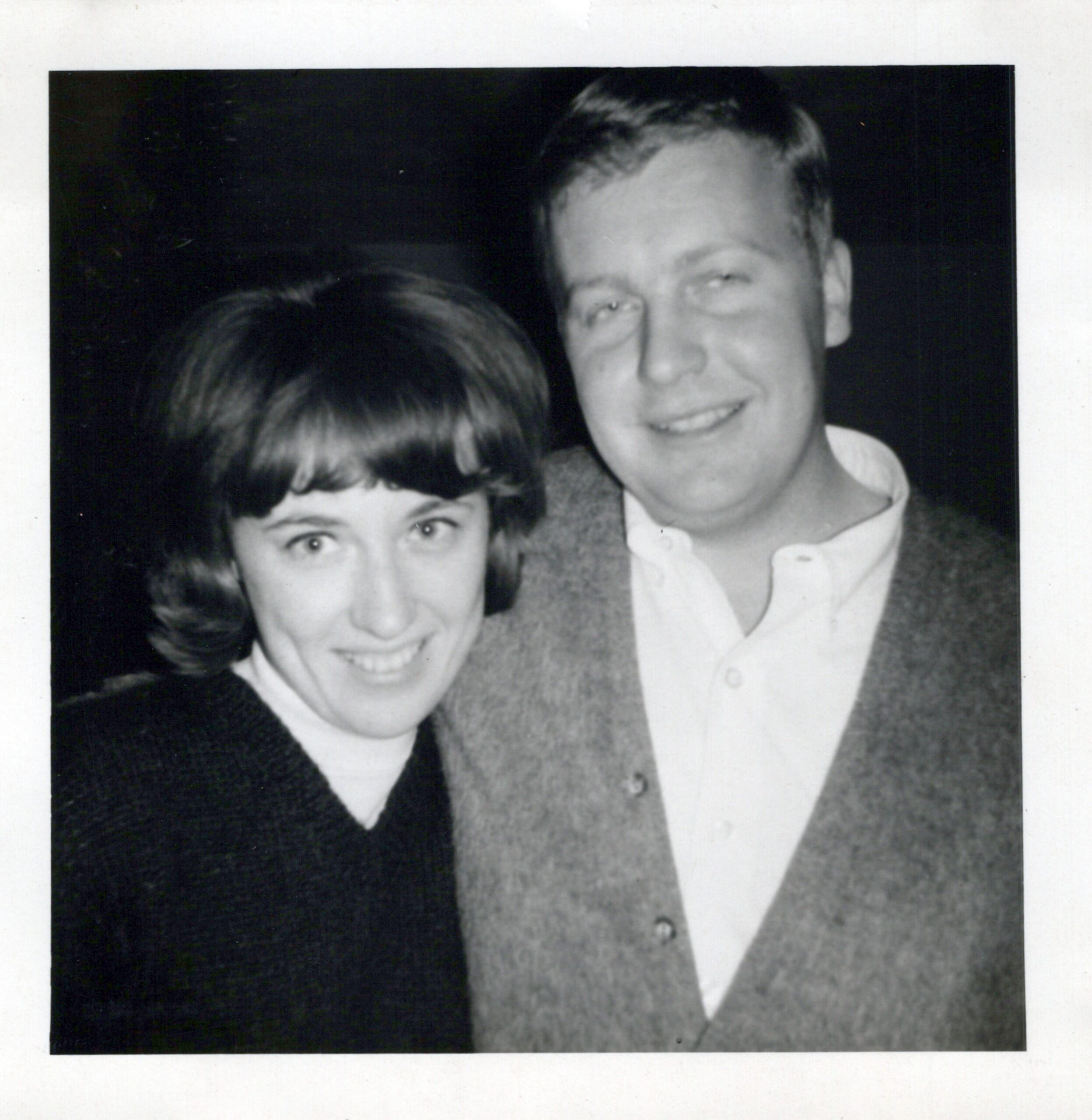 Two people posing closely and smiling for a black-and-white photo, a man on the right and a woman on the left, with their faces partly cropped in.