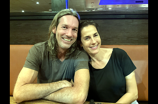 Smiling couple seated at a booth in a restaurant, leaning close together toward the camera.