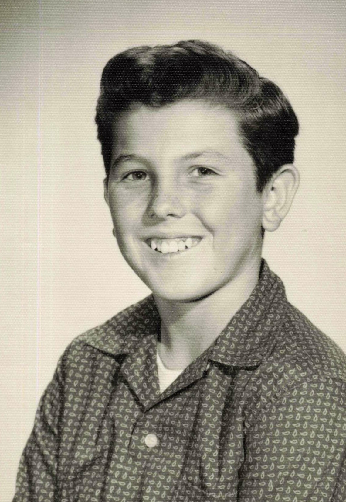 Black-and-white portrait of a smiling boy wearing a patterned button-up shirt.