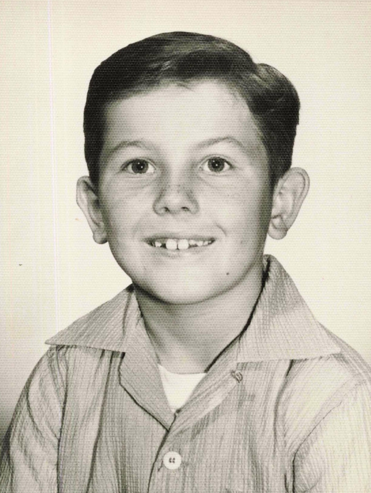 Black-and-white portrait of a smiling boy with short dark hair wearing a striped collared shirt.