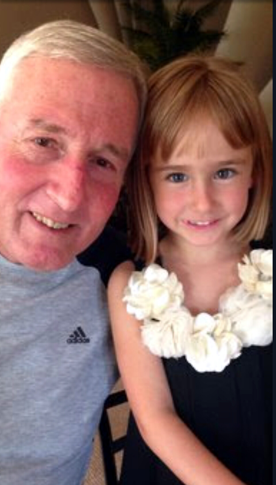 Older man and young girl smiling for a selfie; the girl wears a white flower lei.