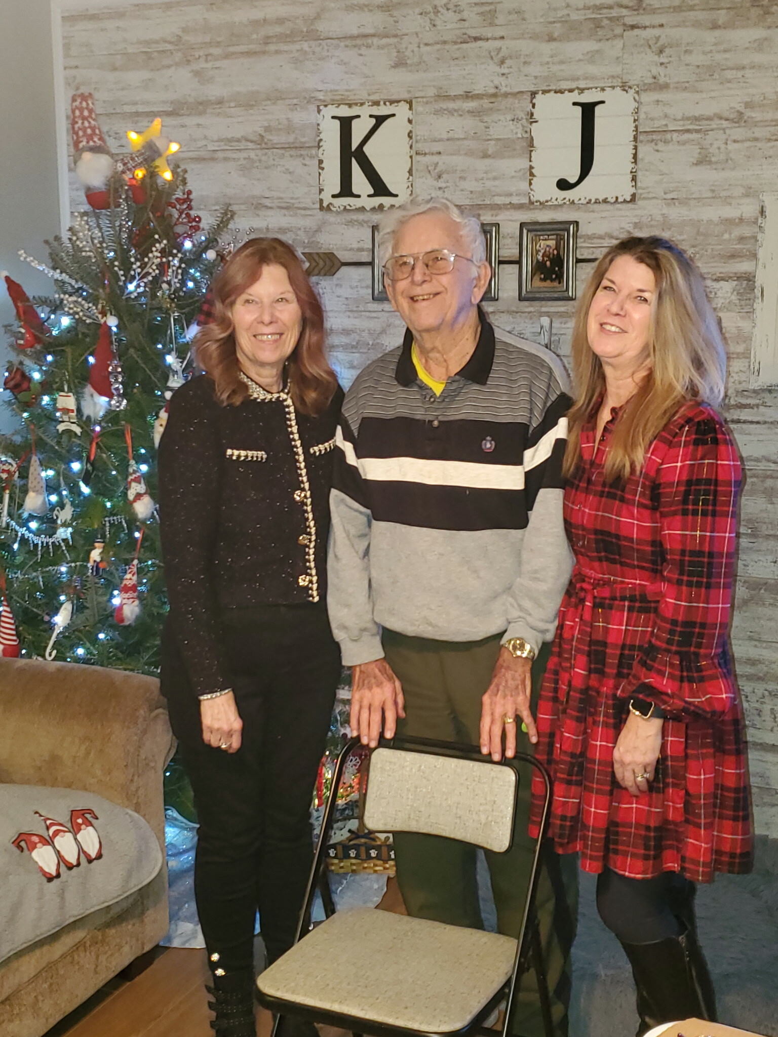 Three adults posing and smiling indoors beside a decorated Christmas tree.