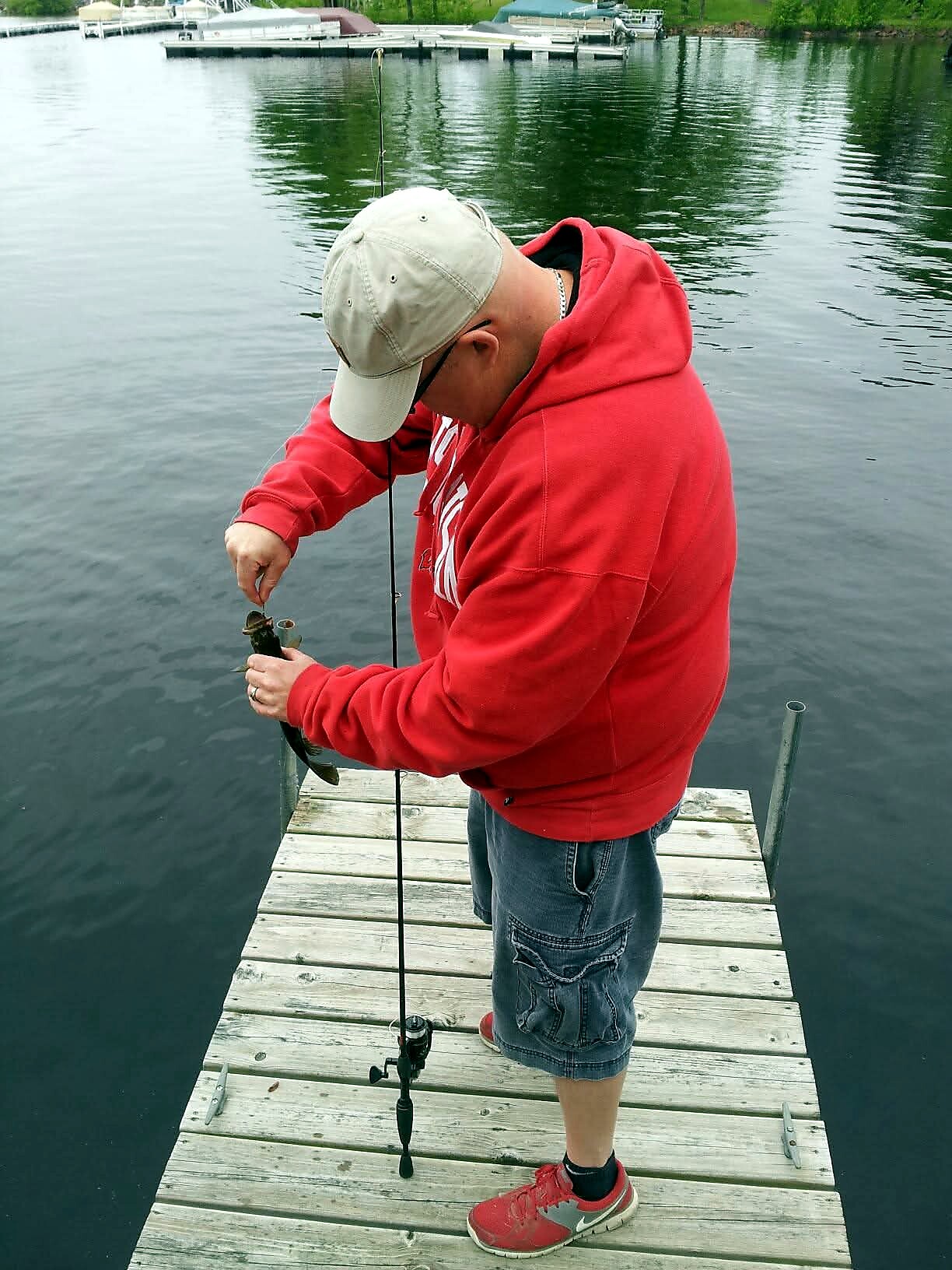 Person on a wooden dock by a calm lake, holding a rod and a small caught fish.