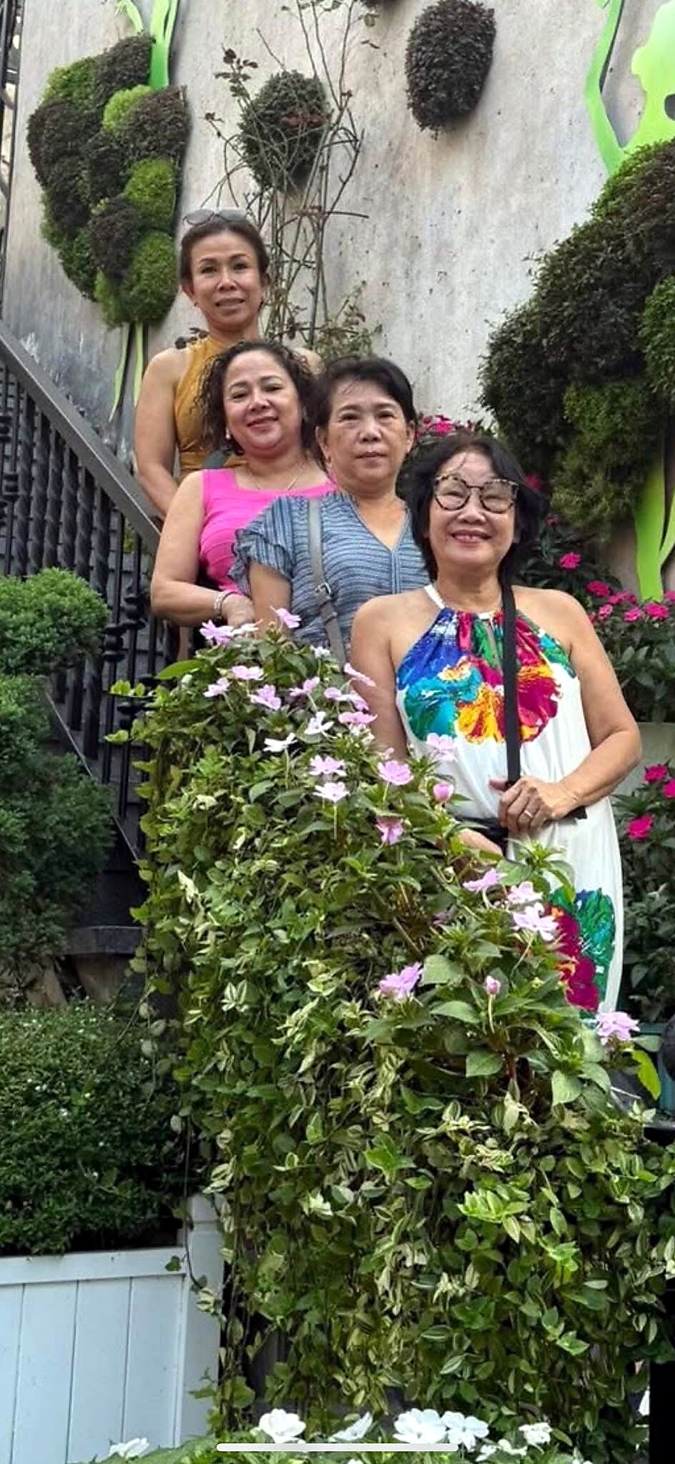 Four women posing on a stairway bordered by green shrubs in a garden.