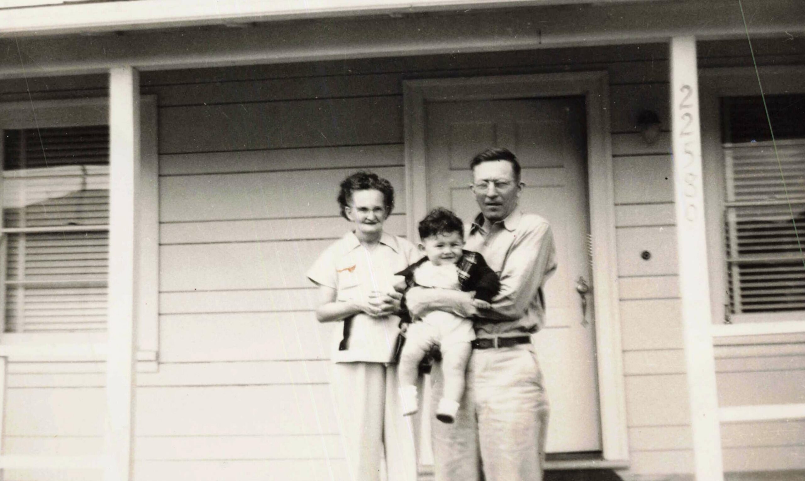 Family of two adults and a child standing on the front porch of a house.
