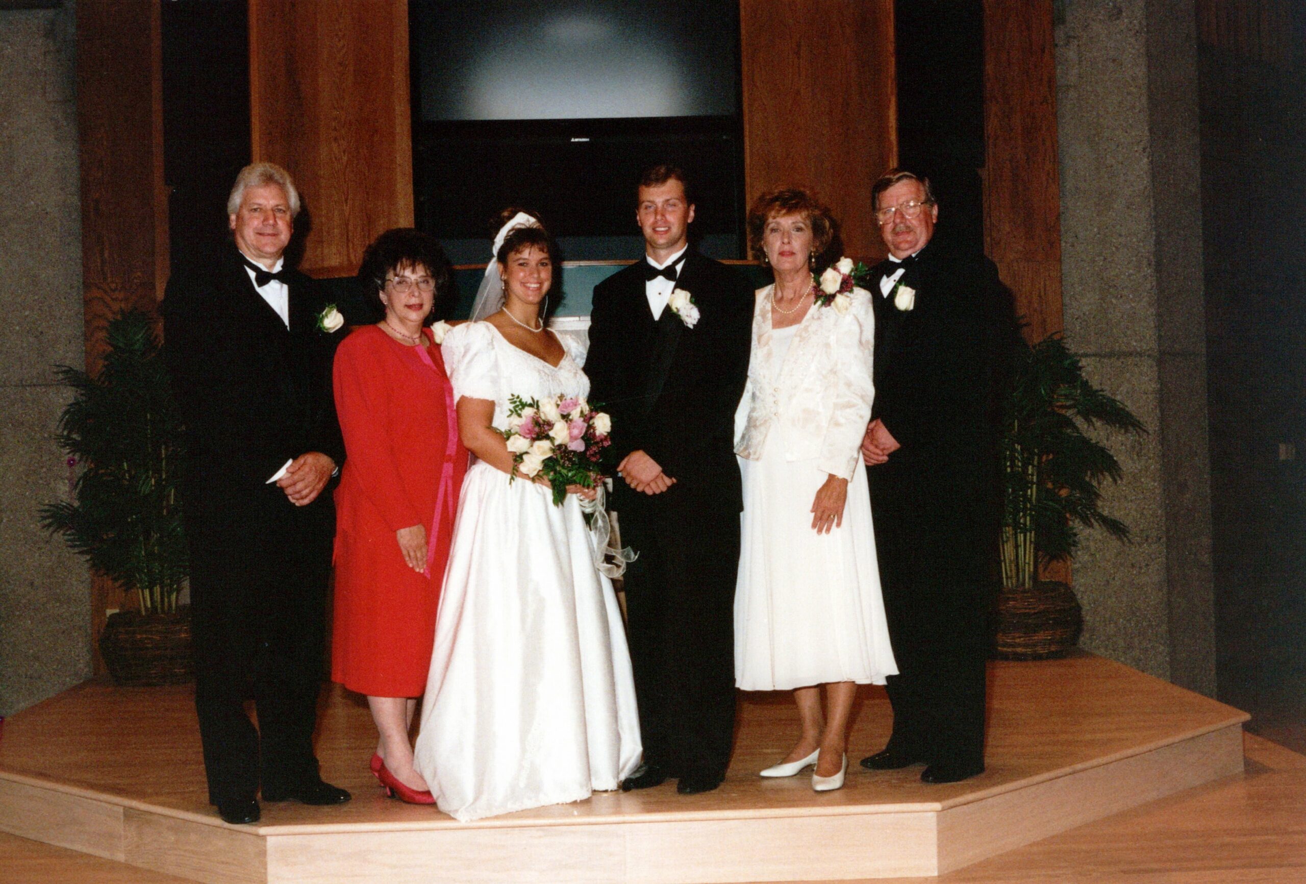 Bride and groom with family members in formal wear posing on a church stage.