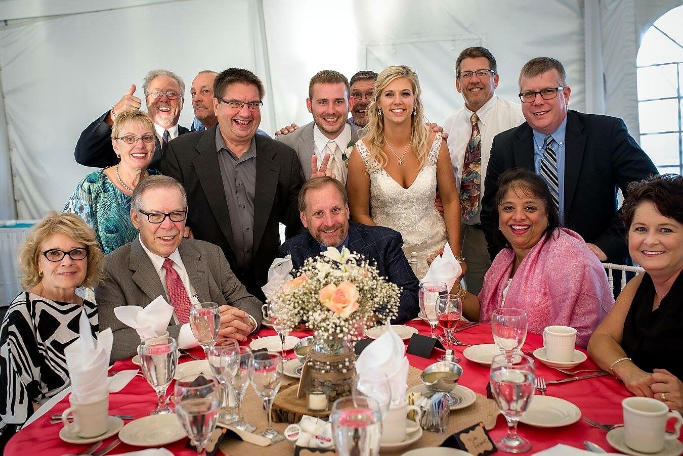 Bride and groom posing with family and friends around a decorated reception table indoors.
