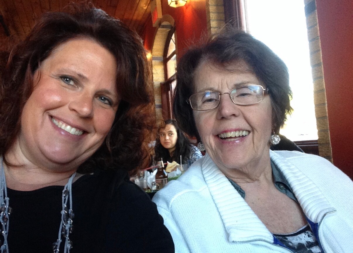Two women smiling for a selfie at a restaurant table with drinks in the background.