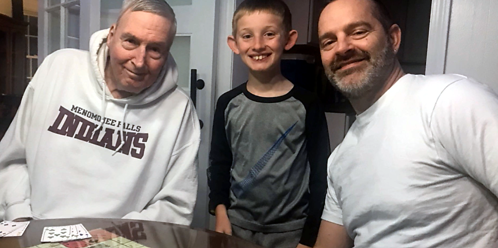 Three people, two adults and a child, smiling at a table with playing cards laid out in front of them — family game moment.