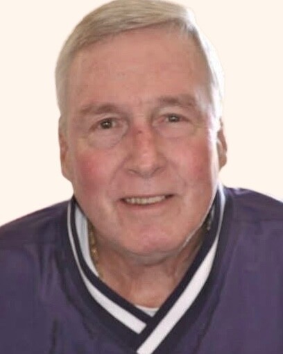 Smiling older man with short gray hair wearing a purple shirt with a white-striped collar.