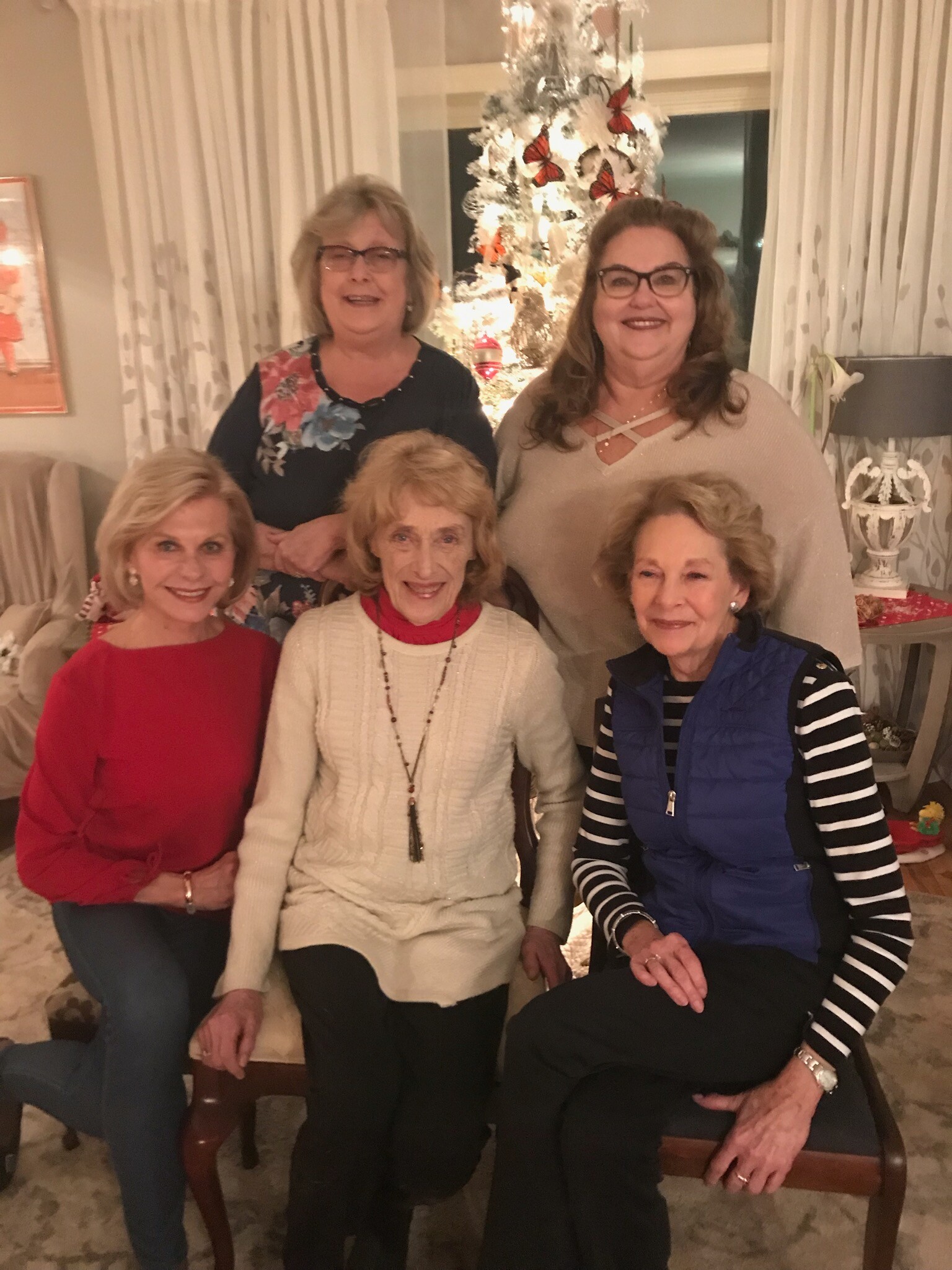 Five women posing together in a living room with a decorated Christmas tree in the background, all smiling.