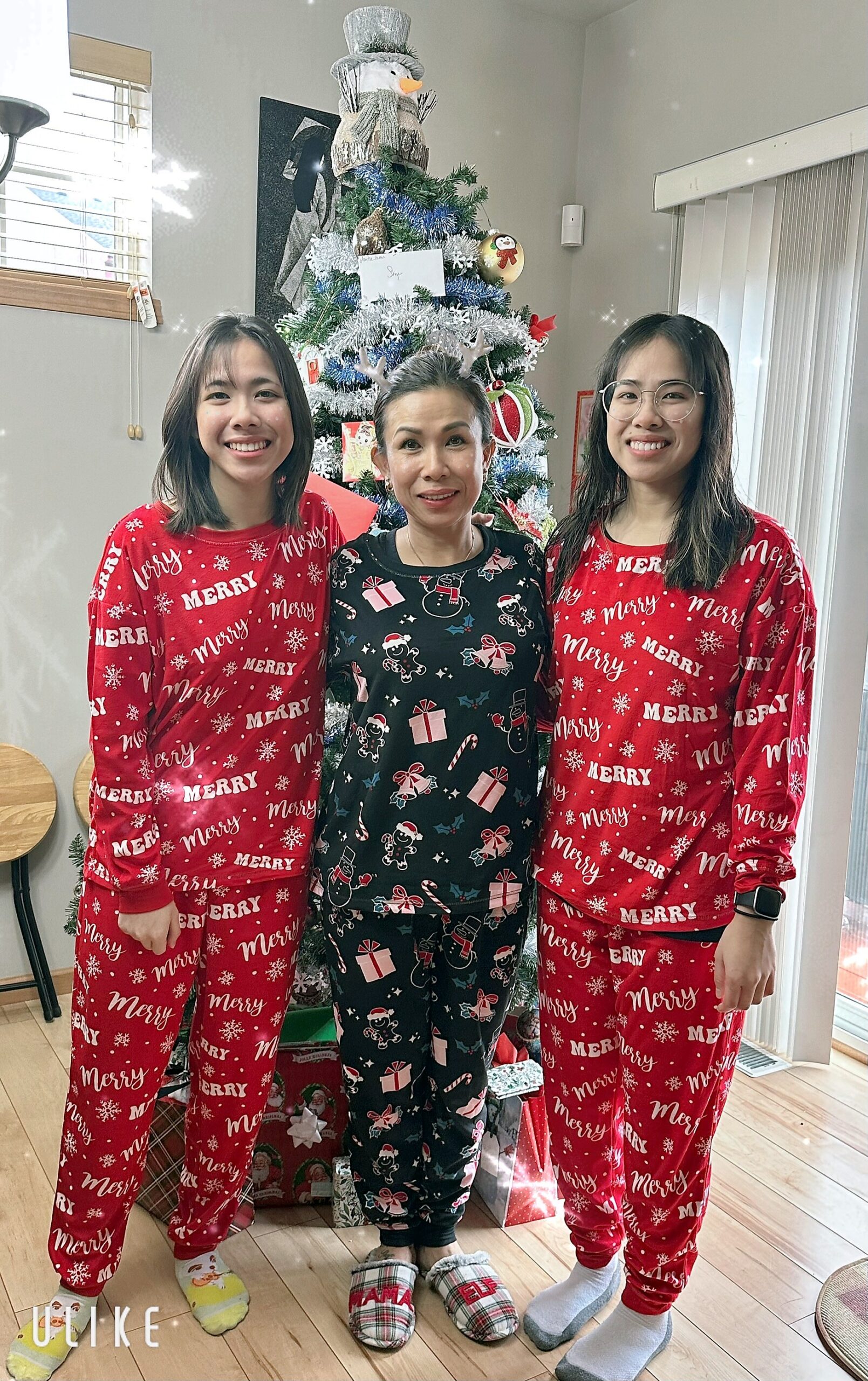 Three women in Christmas pajamas pose by a decorated Christmas tree with a snowman topper in a living room.