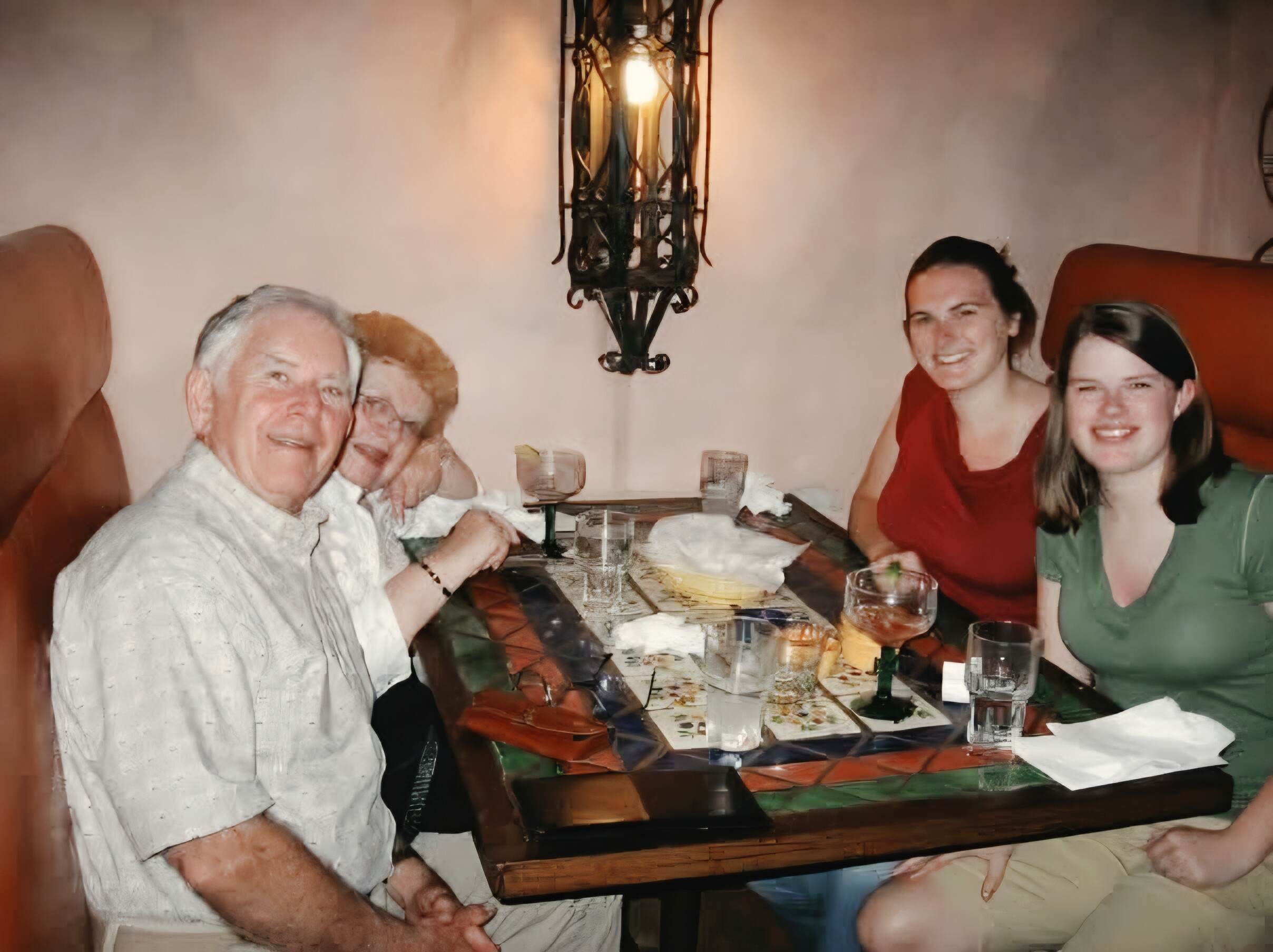 Group of people sitting around a dining table, smiling for a photo during a meal in a cozy restaurant setting with drinks and plates visible.