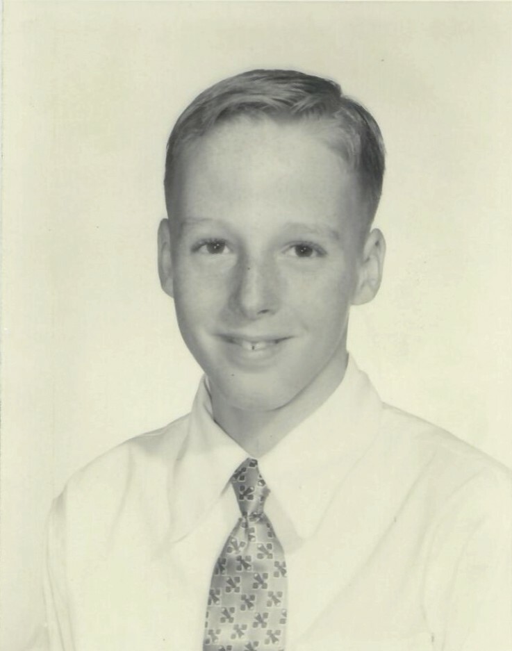 Smiling boy in a dress shirt and patterned tie, posing for a formal portrait at school.