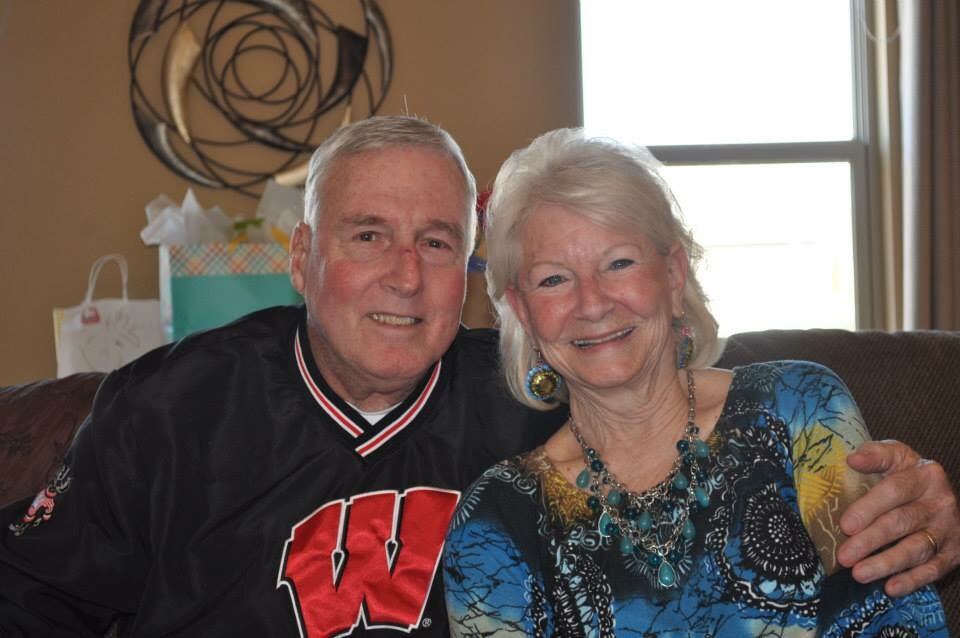 Man in a black jacket with a large red 'W' sits close to a smiling woman on a sofa, both facing the camera.