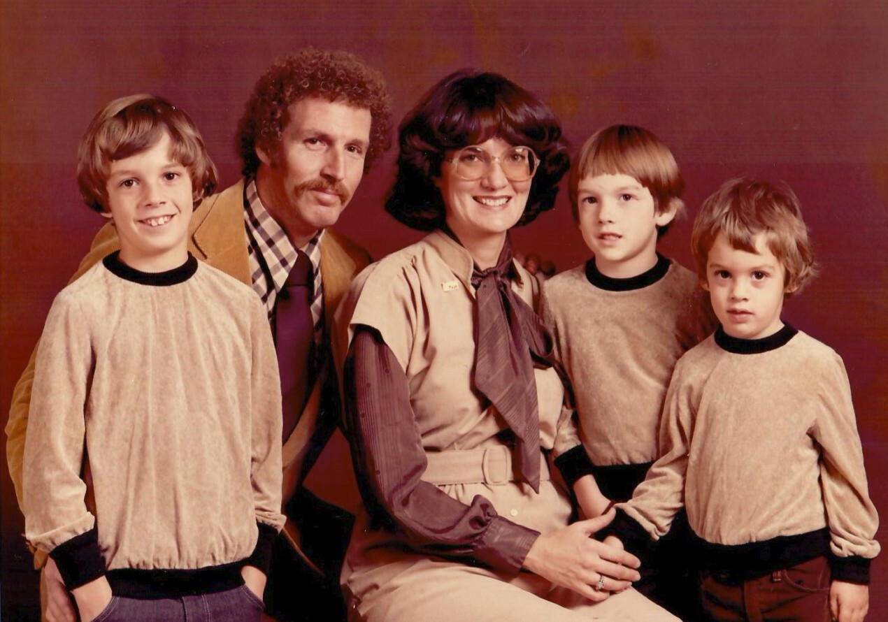A family portrait: mother and father seated with their three young sons standing beside them, all smiling in 1970s-style clothing.