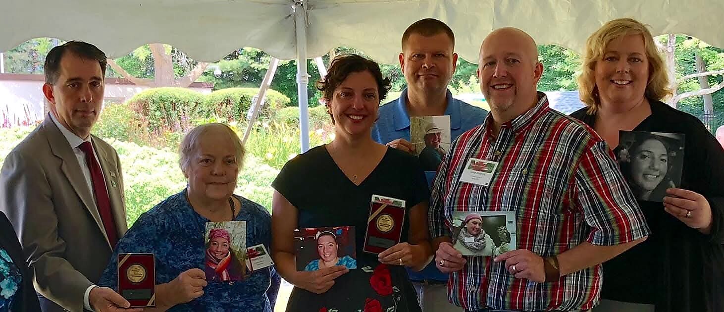 Six adults under a canopy pose for a photo, each holding portraits or awards.