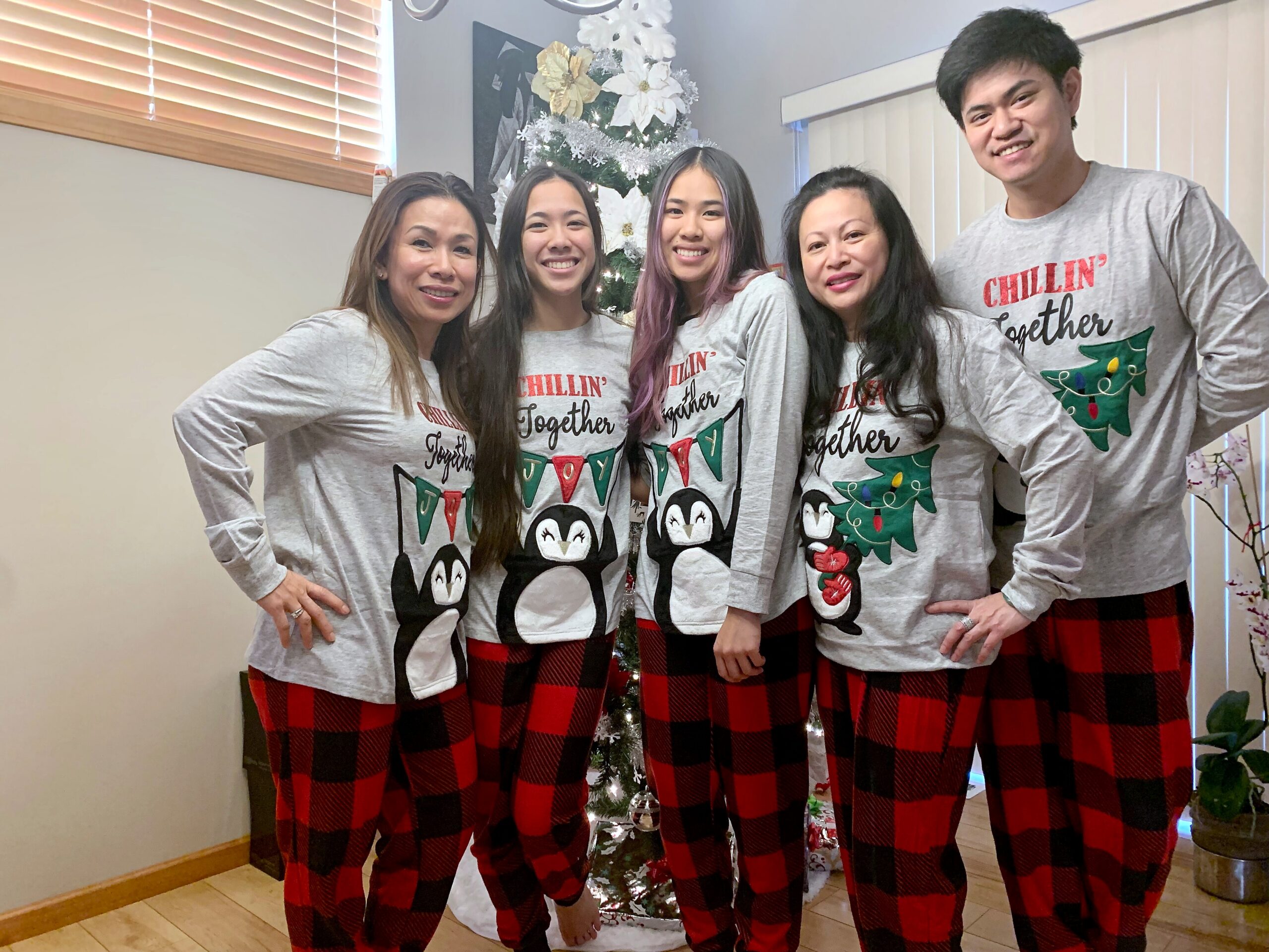 Group of five people in matching gray 'Chillin' Together' shirts and red plaid pants posing in a living room with a Christmas tree behind them, smiling.