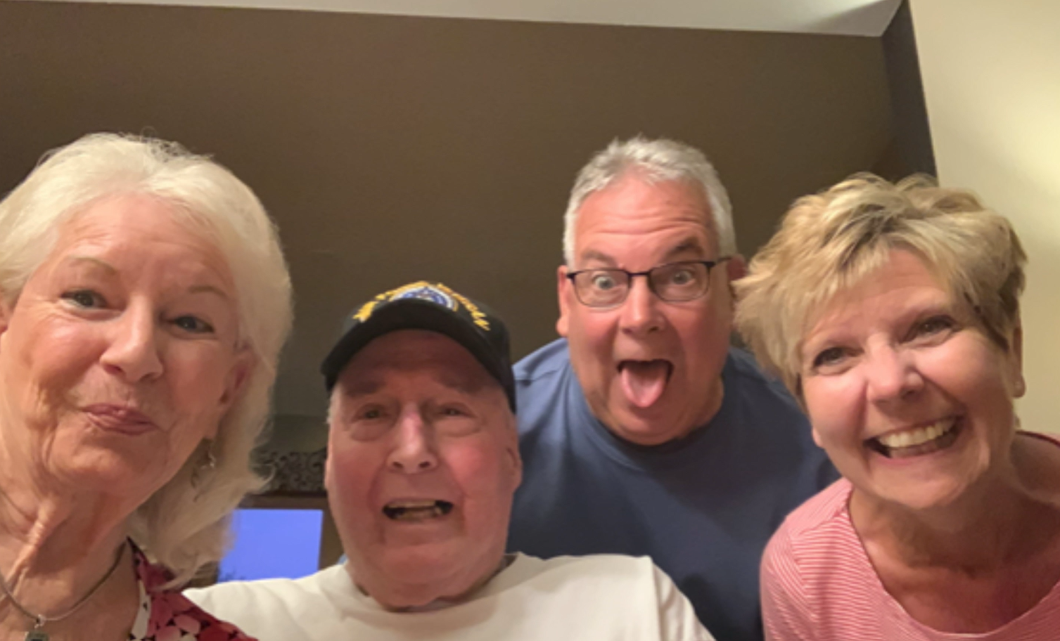 Four adults taking a cheerful selfie indoors, smiling at the camera.