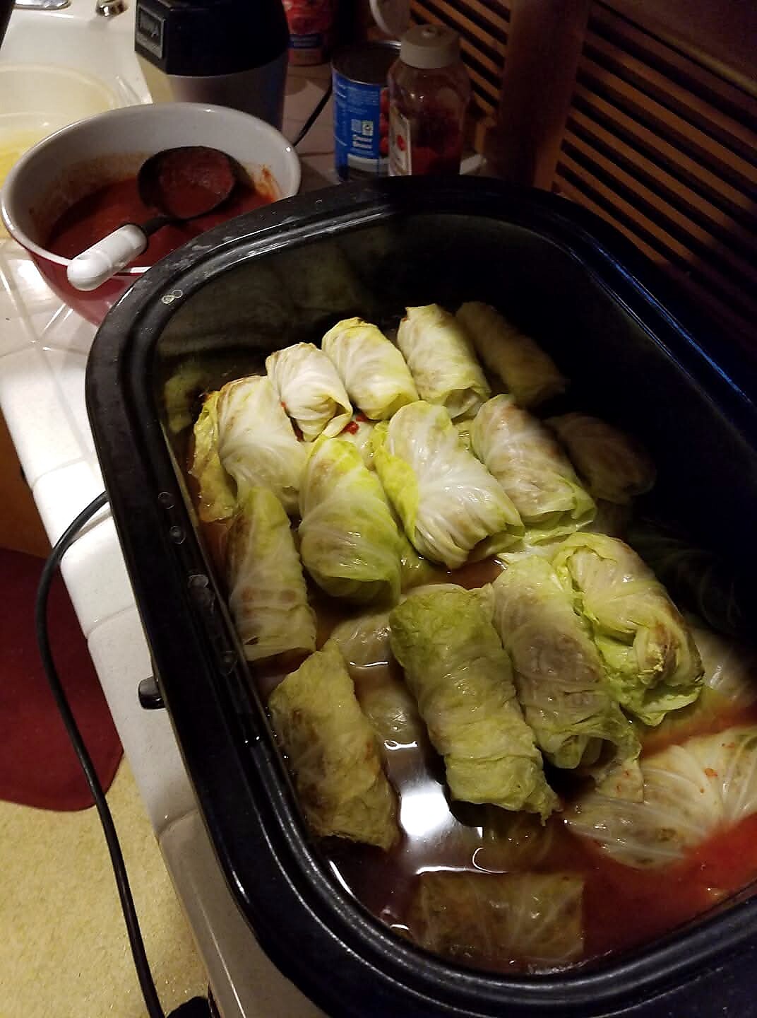 Cabbage rolls arranged in a slow cooker with tomato sauce underneath, ready to cook or warm.